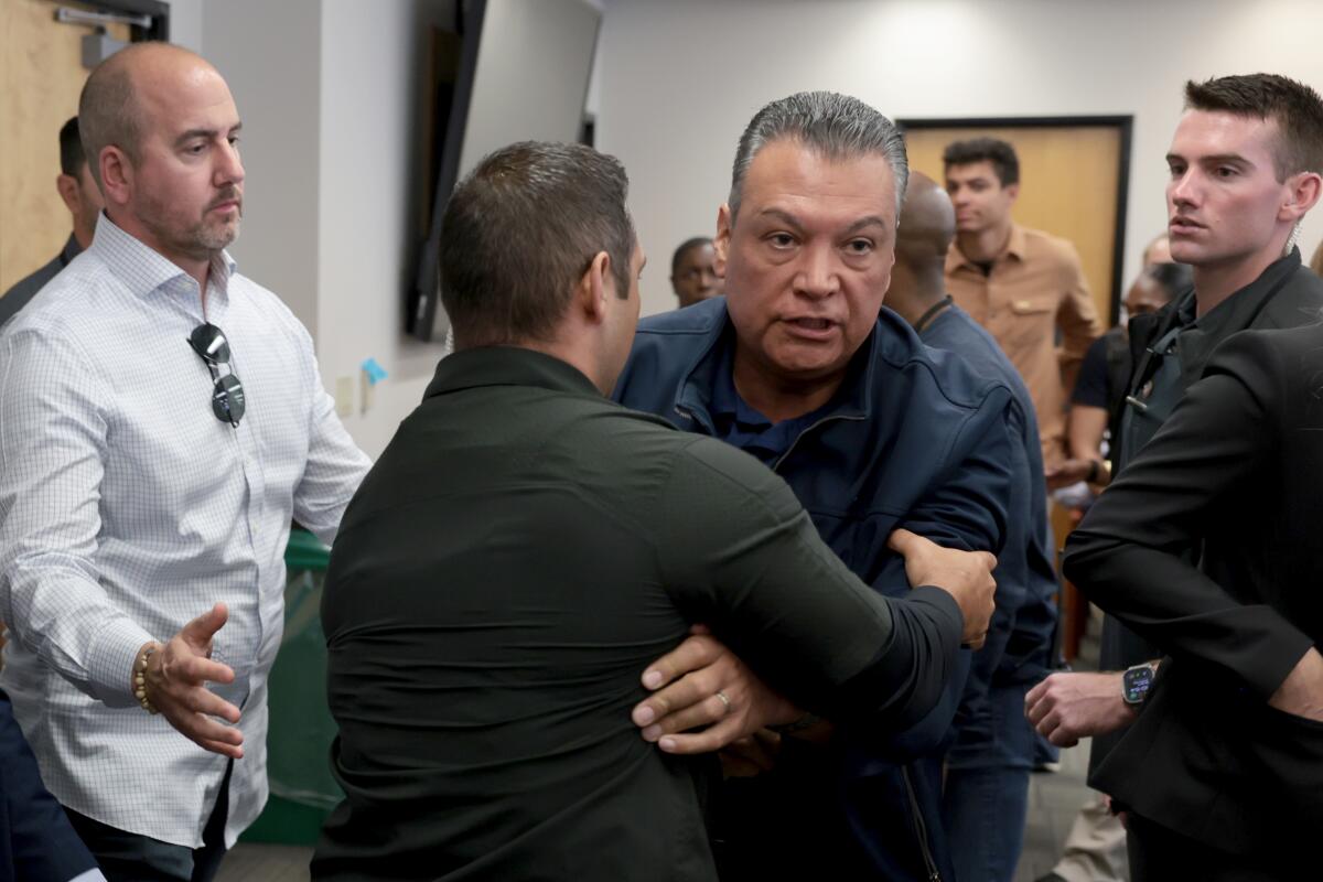 Sen. Alex Padilla is removed from a room by another man.