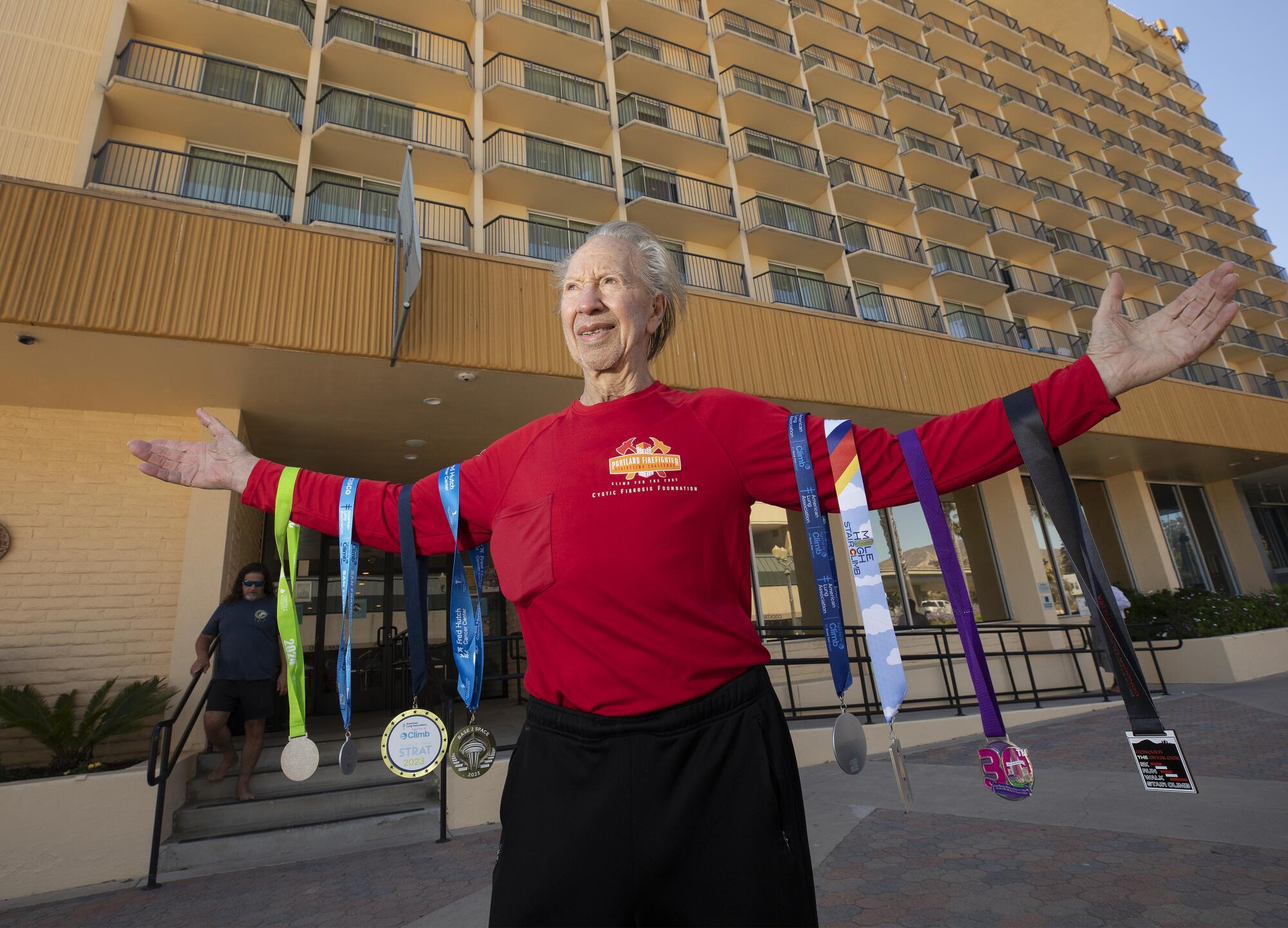 A man stands outside a hotel with four race medals hanging from each arm. 