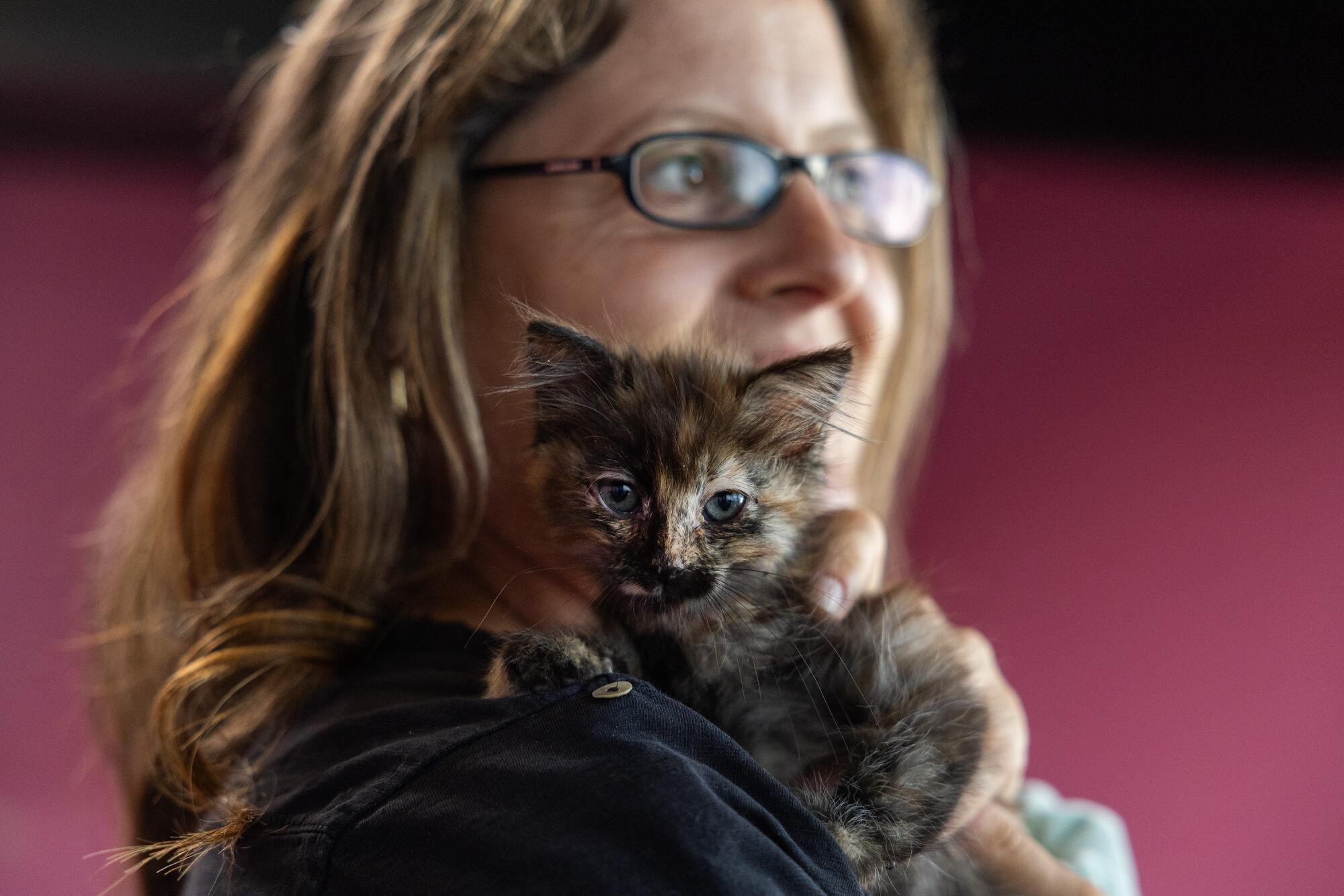 A woman holds a kitten on her shoulder.