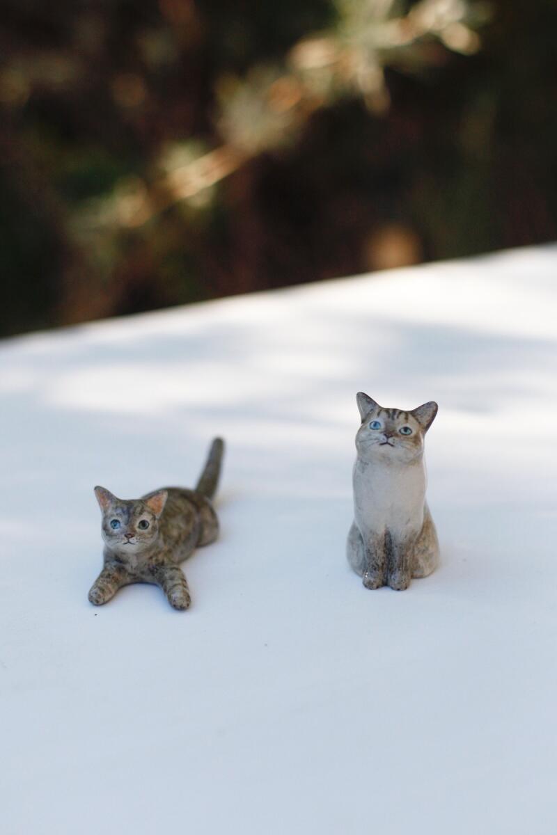 Two custom cat figurines rest next to one another on a table 