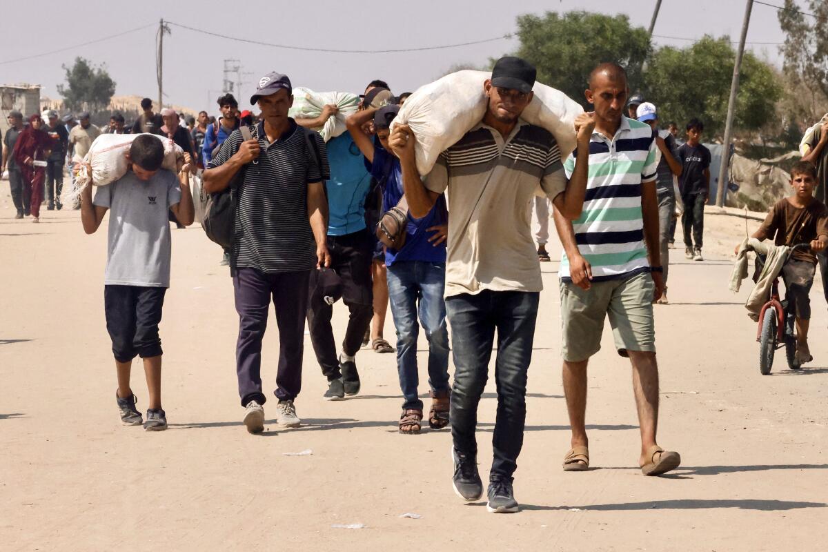 Men walk carrying bags on their shoulders.