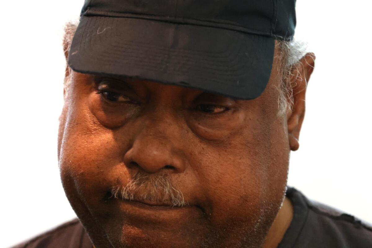 A man with a gray mustache, in a dark cap