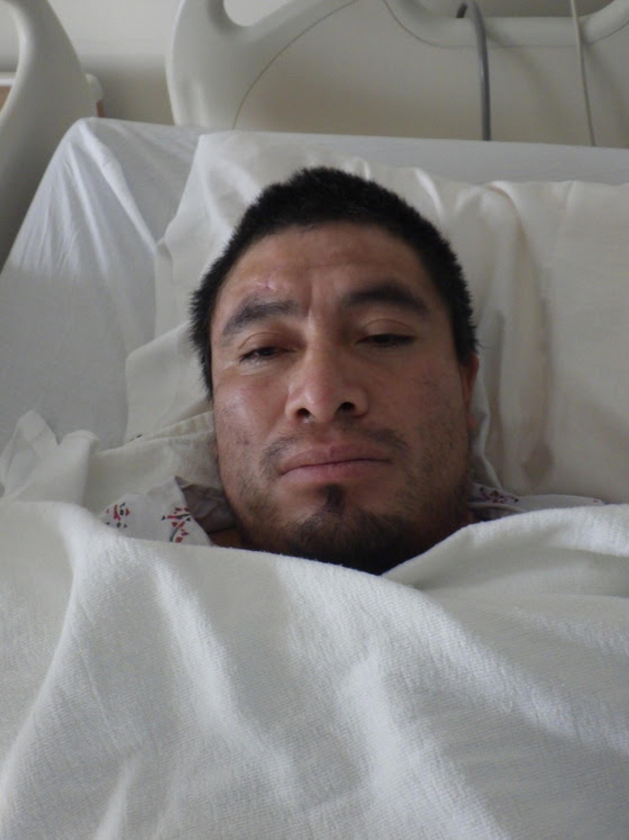 A man lays in a hospital bed looking at the camera.