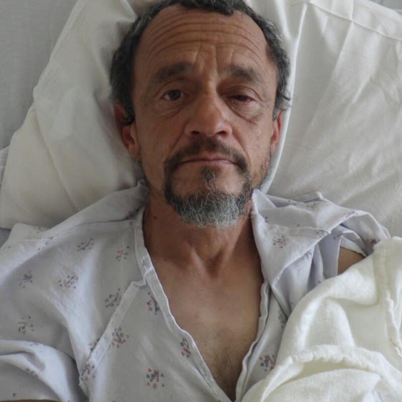 a man lays in a hospital bed and looks into the camera