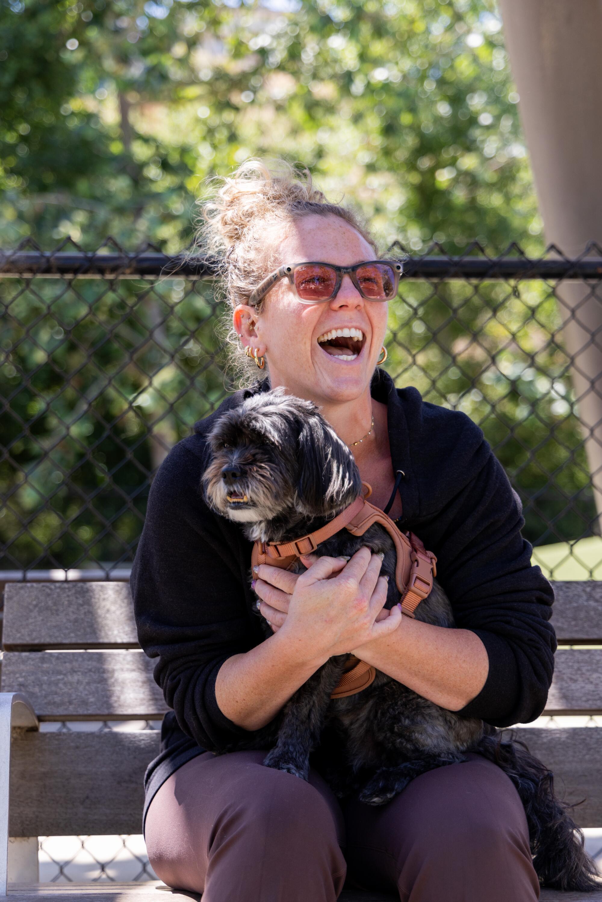 Becca Nelson, in black hoodie and sunglasses, holds her dog Sadie at Bluff Creek Dog Park in Playa Vista.