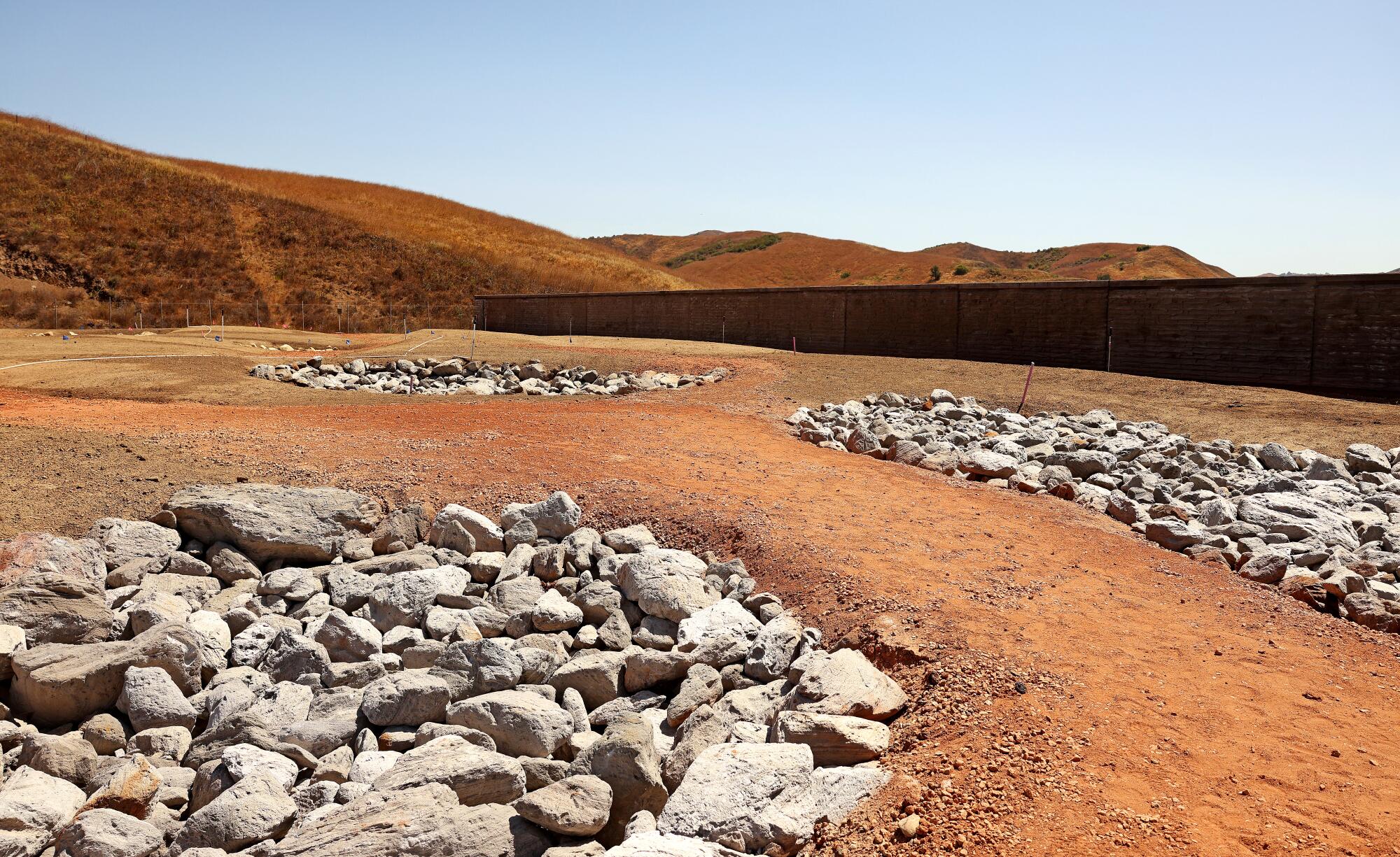 The top of the Wallis Annenberg Wildlife Crossing looks barren with piles of grey rocks and bare reddish soil. 