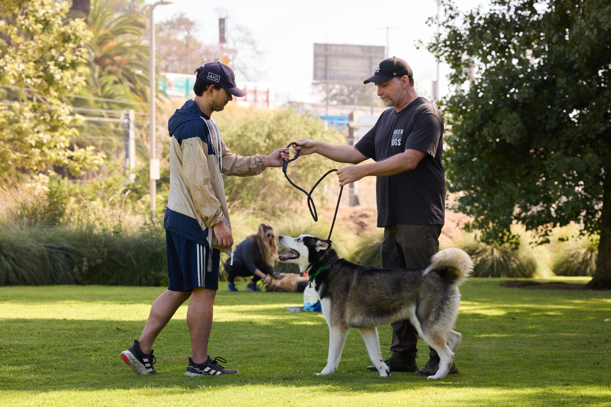 A man hands a husky on a leash to another man in a park. 
