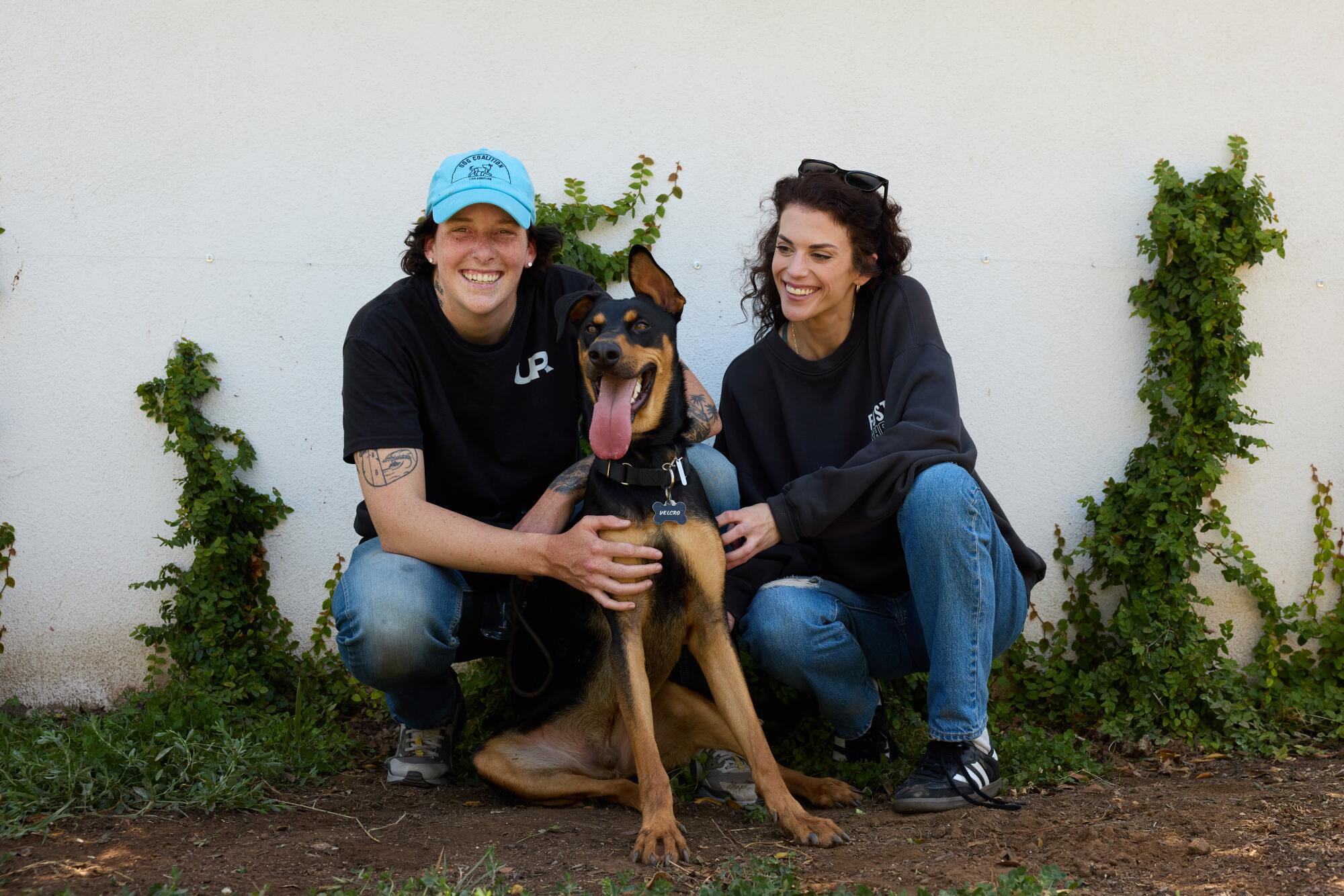 Two women pose next to a black and brown dog.