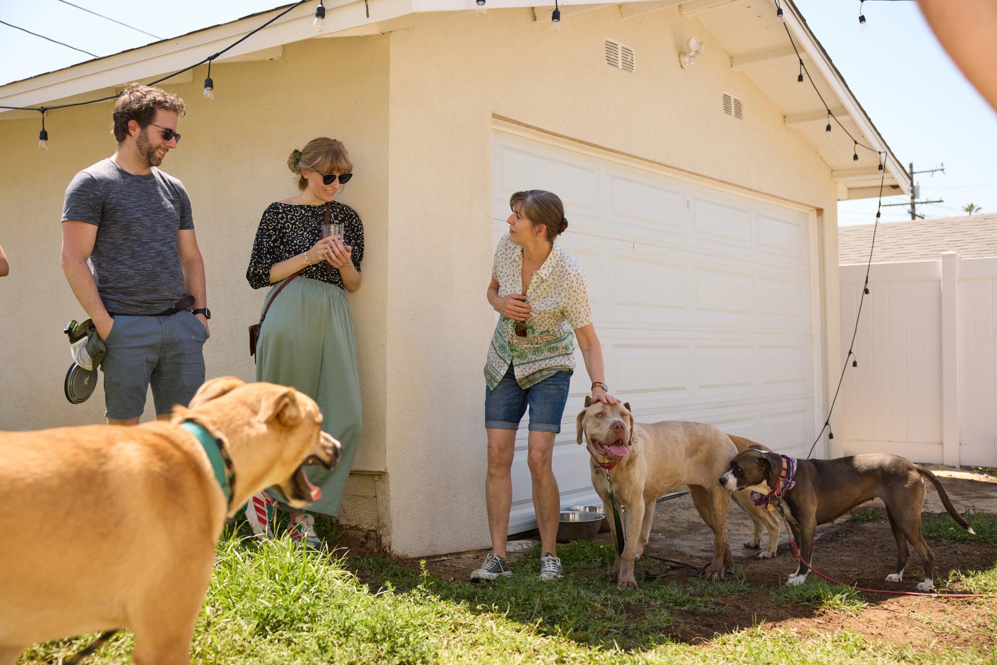 Three people stand near a garage along with two large dogs.