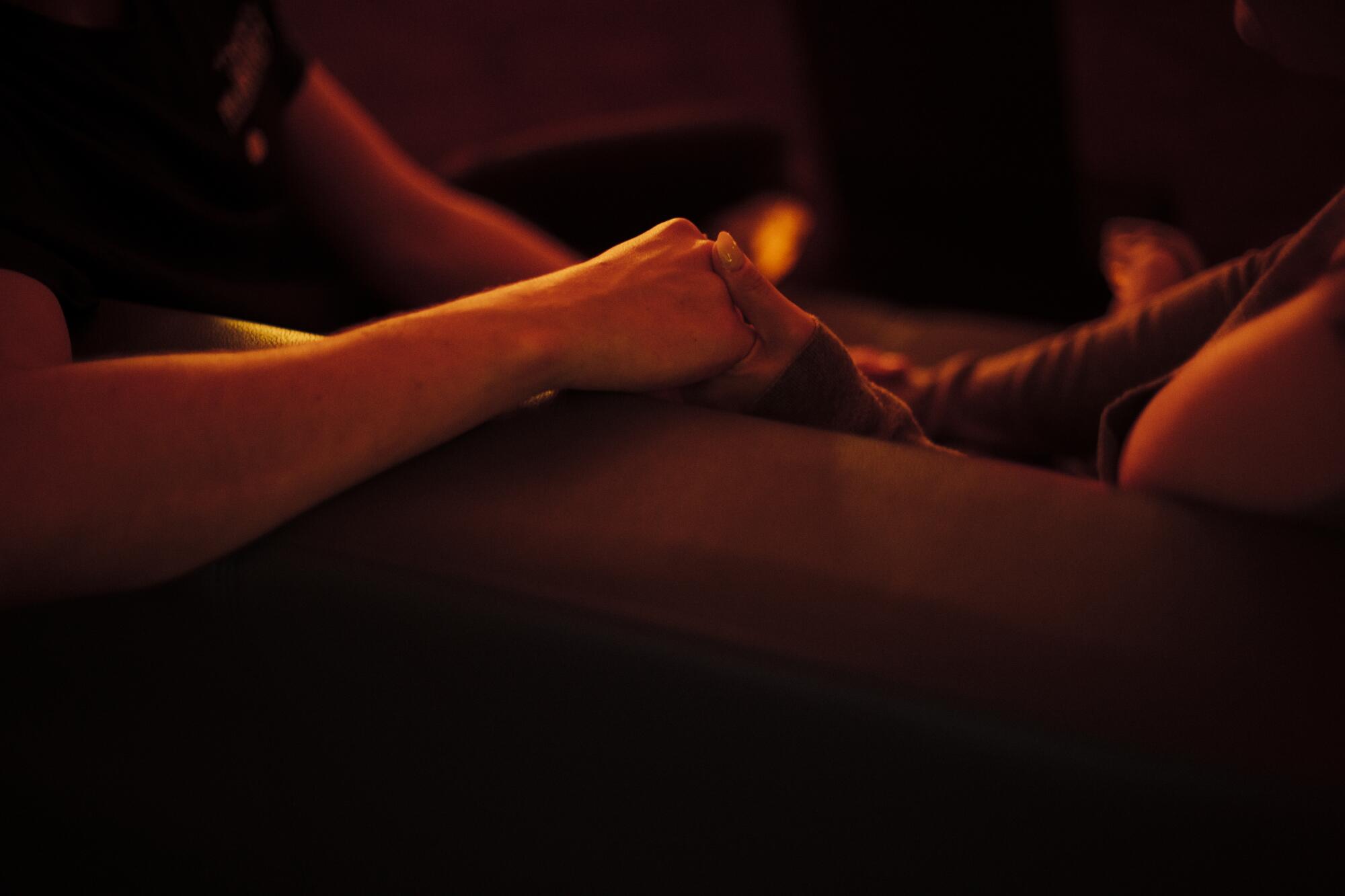 Two hands, clasped, in a candlelit room.