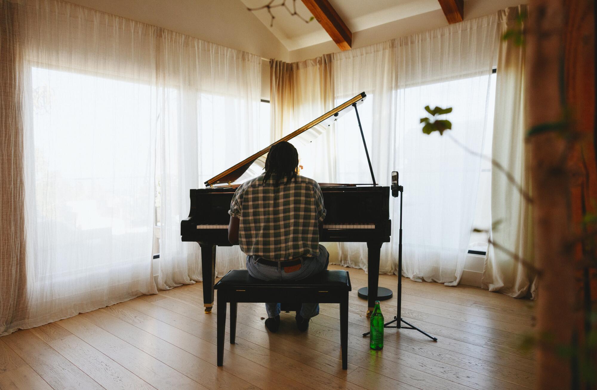 A man's back is seen while he plays at the piano with gauzy drapes in the background.