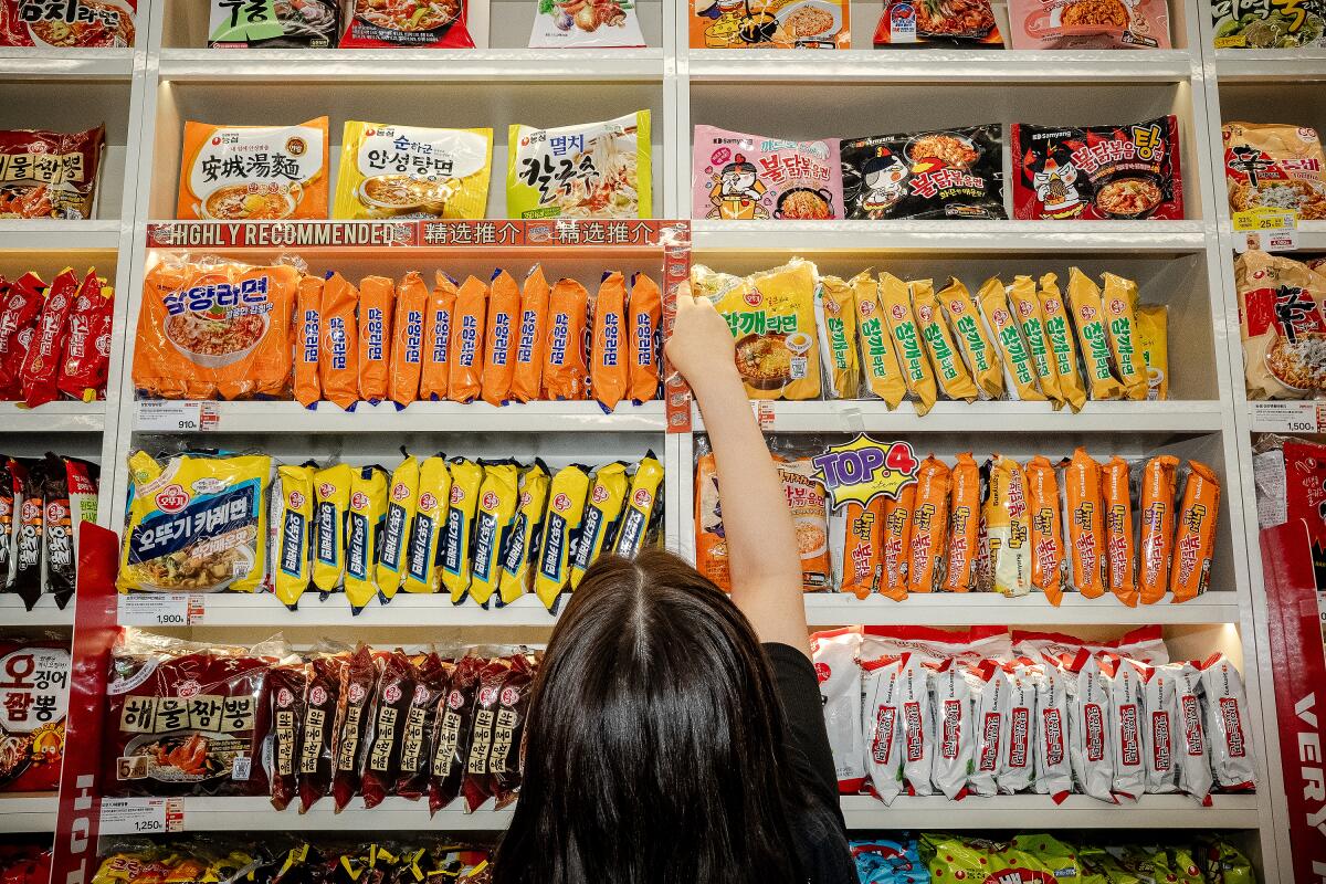 A worker sticks "highly recommended" labels in English and Chinese on the shelf of ramyon.