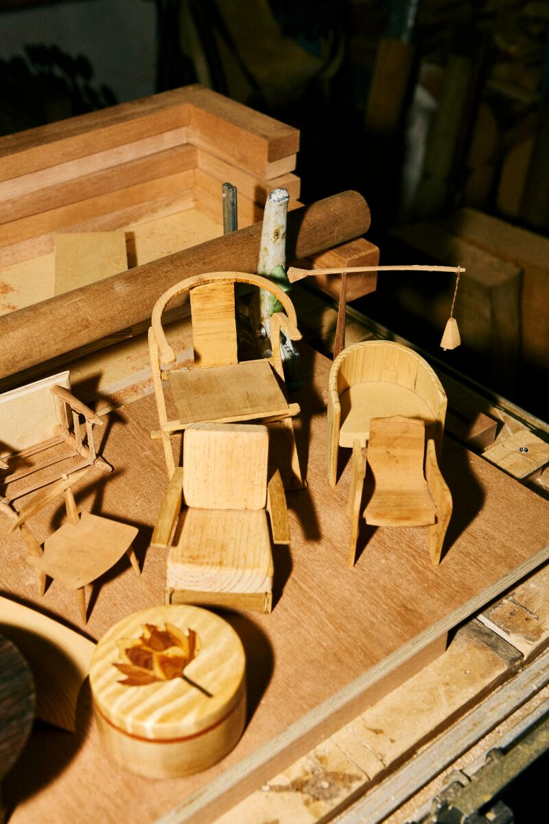 Miniature lamp and chairs sit on a piece of wood.