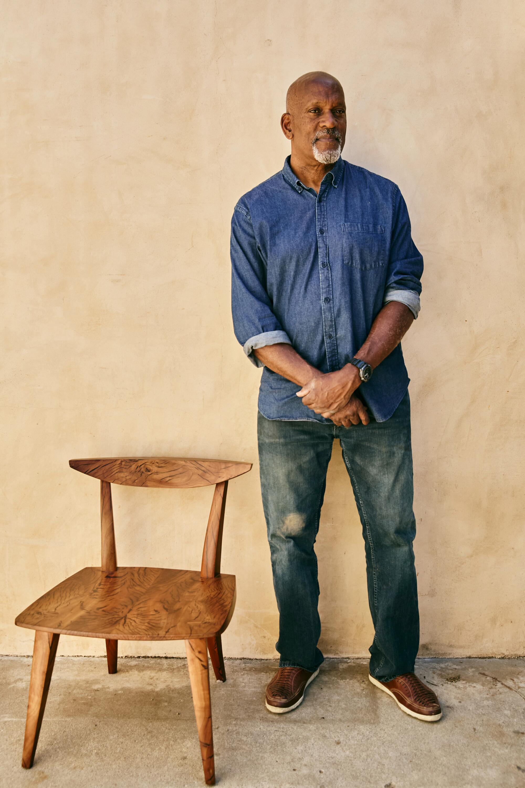 Man stands next to chair up against a wall.