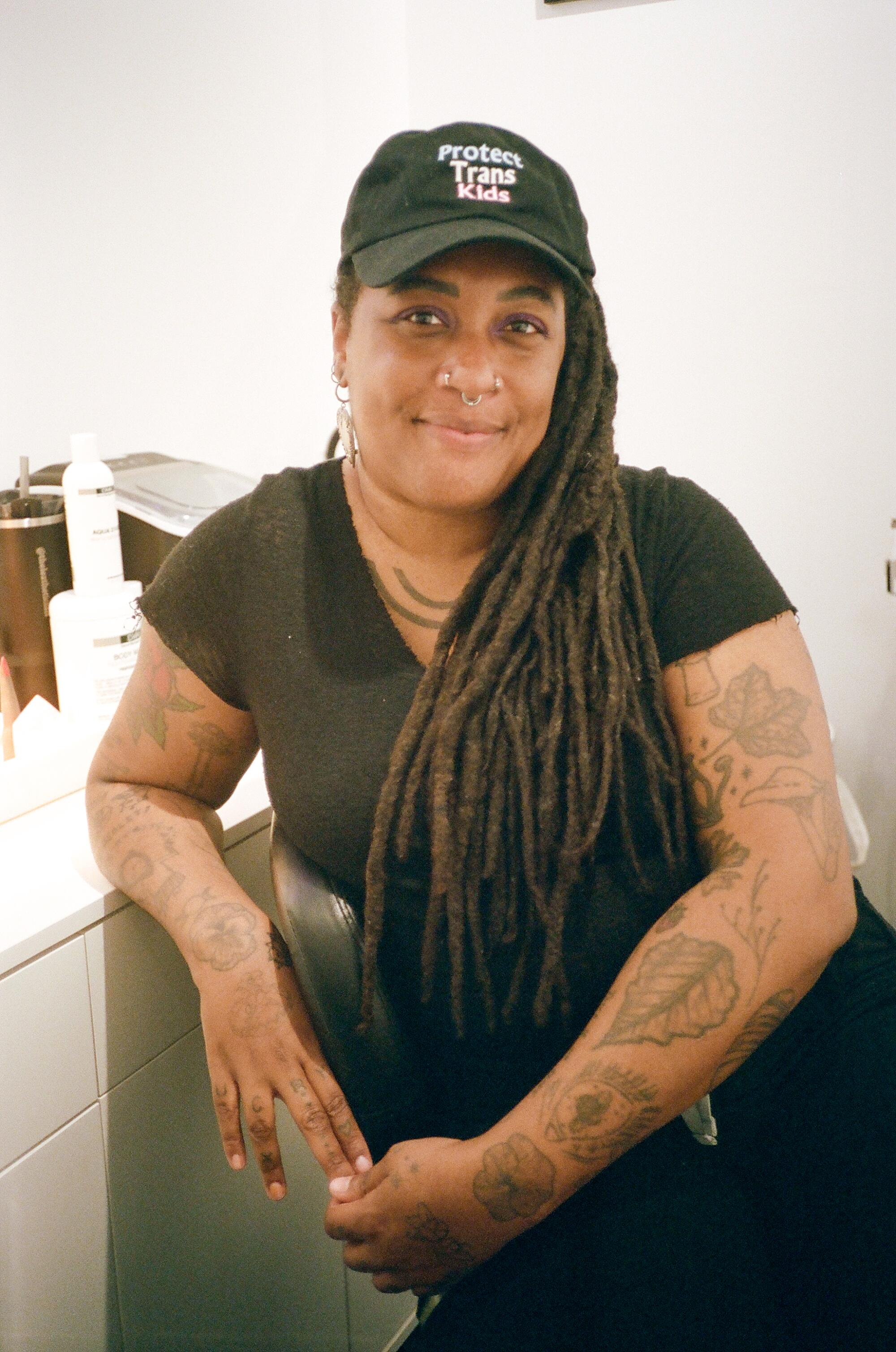 A person sitting in a chair wearing a black top and a baseball cap.