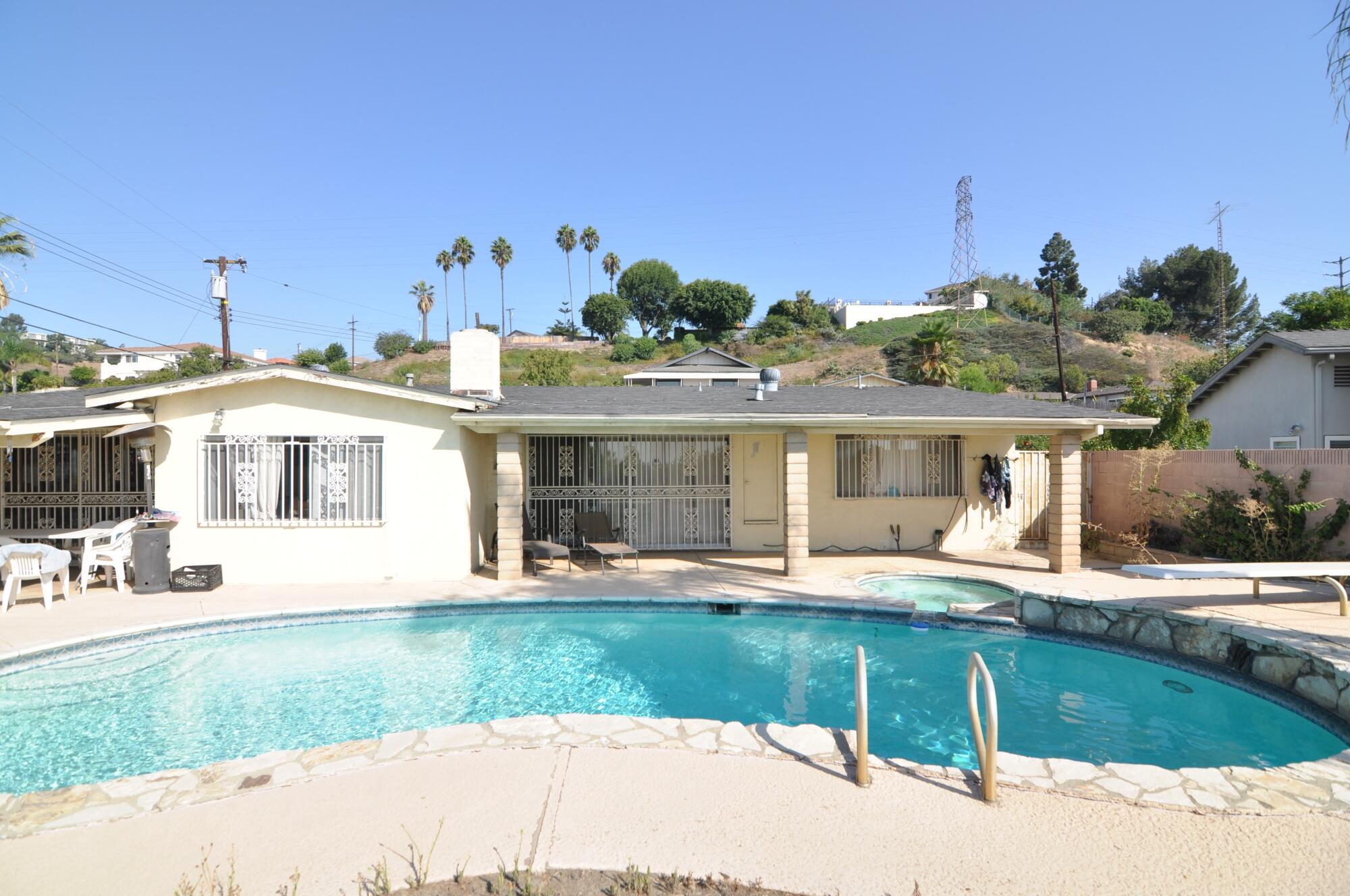 A white Midcentury home with bars on the windows and a pool in foreground.