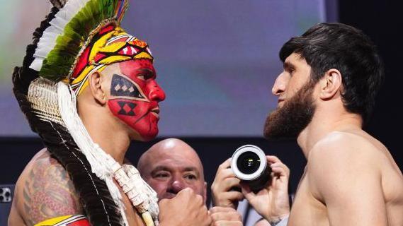 Alex Pereira, with red face paint and wearing a native hat of Brazil, faces off Magomed Ankalaev
