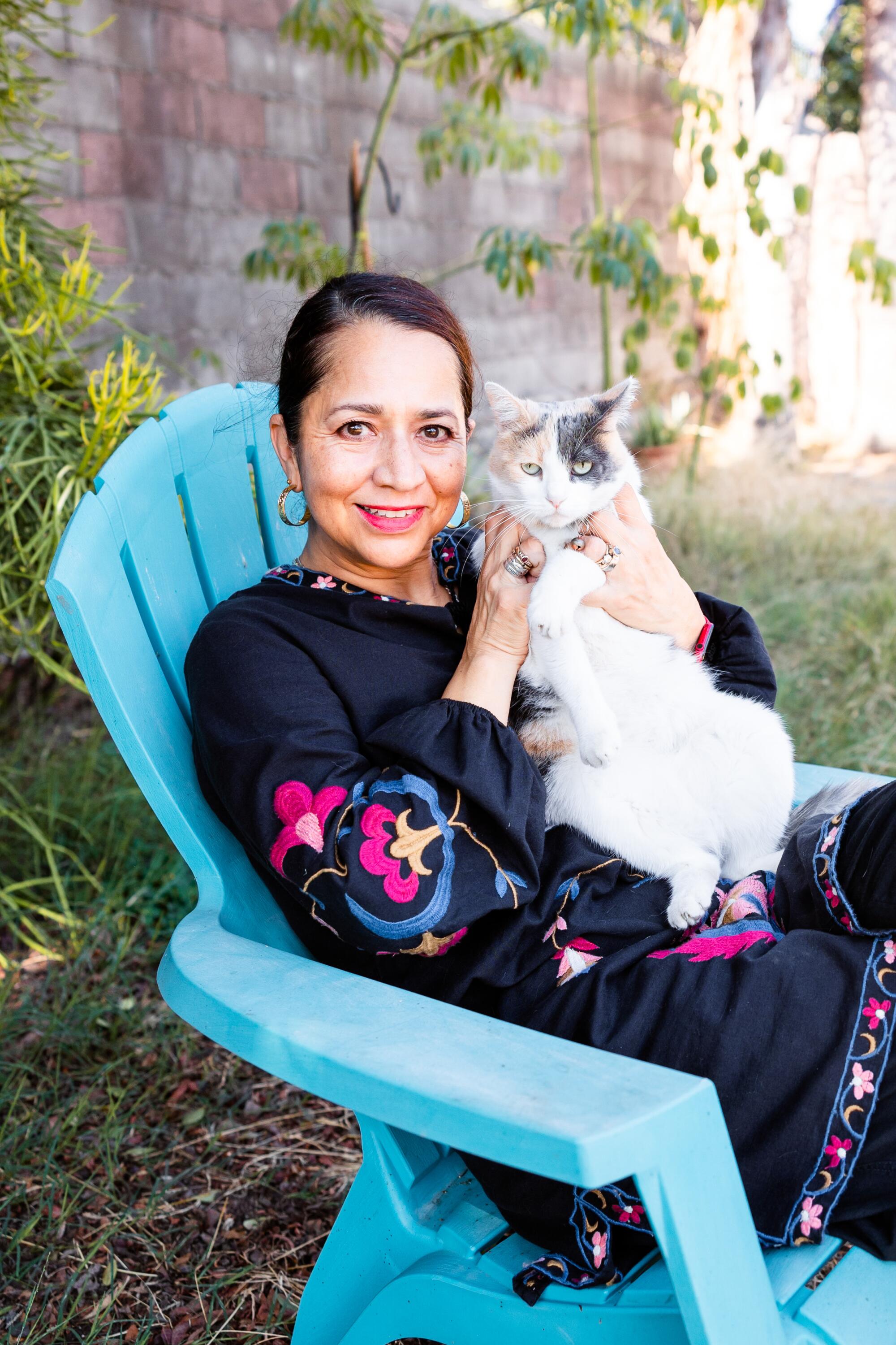 A woman holds her white calico cat in a blue chair.