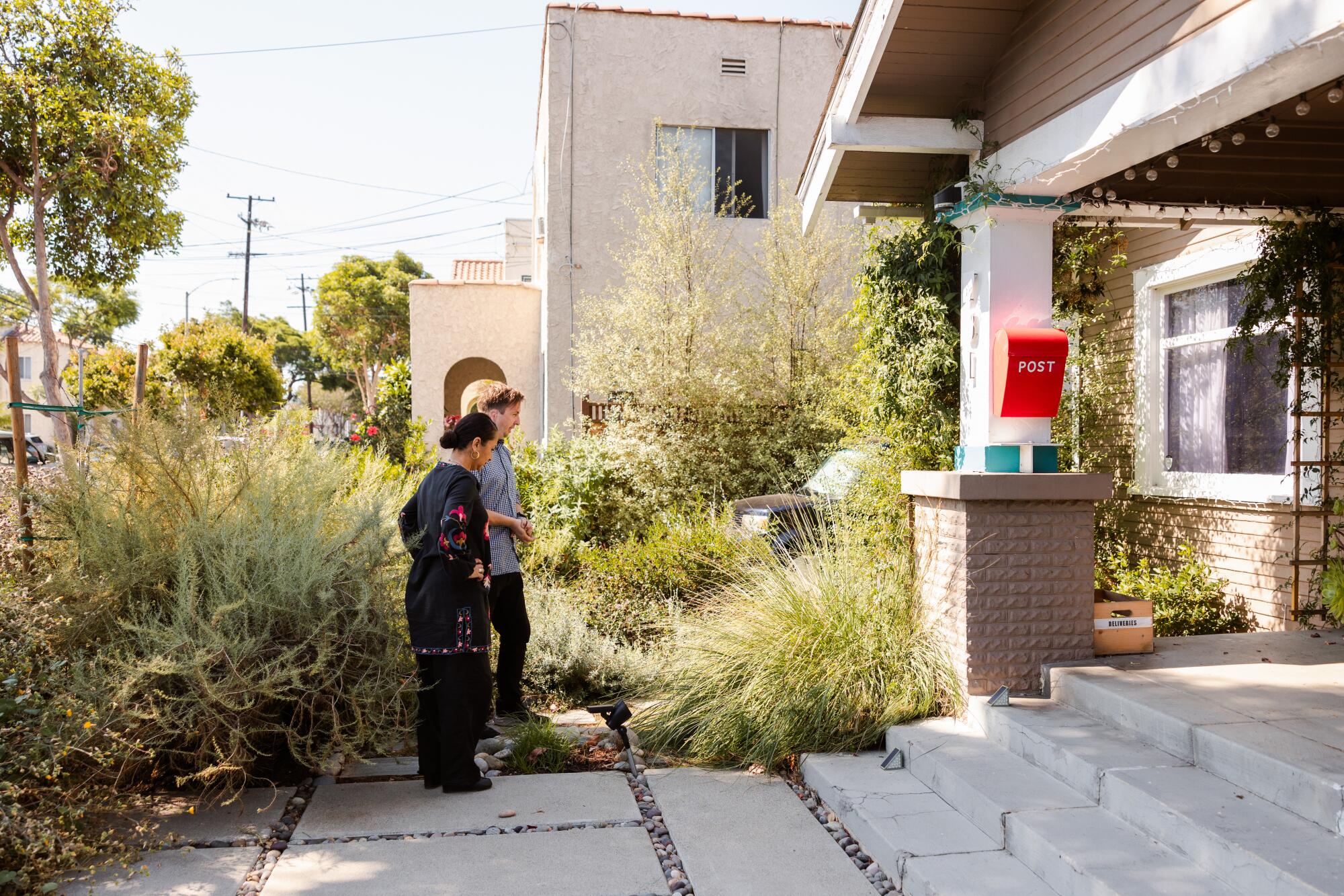 A woman and man admire a lush planting of native grasses and shrubs near the broad porch outside their Long Beach home.