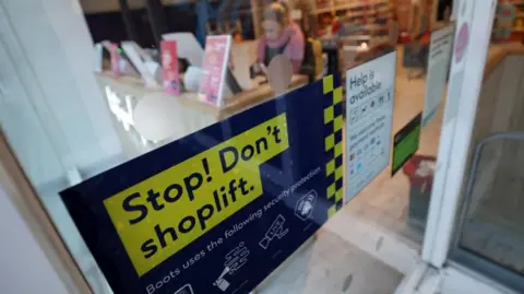 EPA A sign in a shop window says 'Stop! Don't shoplift. Boots uses the following security protection'. A blurred out customer can be seen using a self service till inside the store.