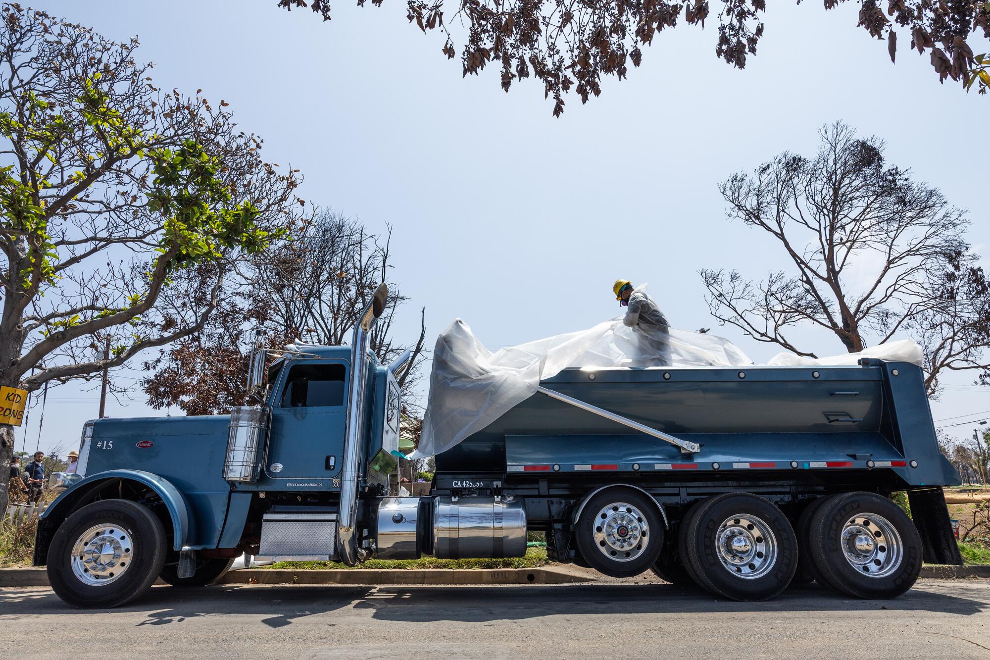 A worker folds and tapes a tarp in a truck