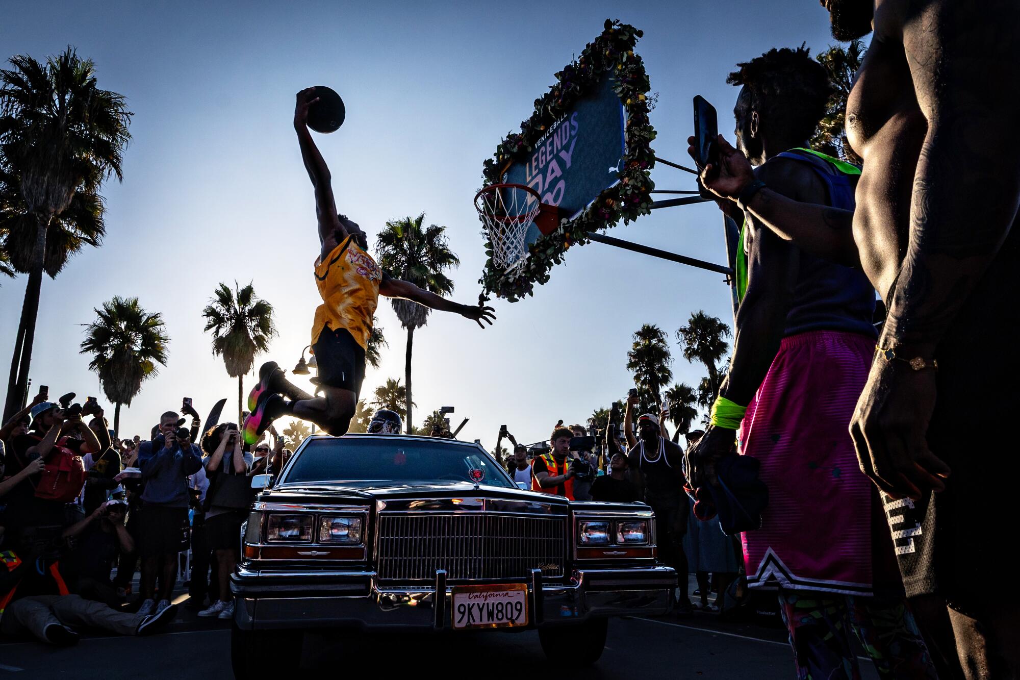 Chris Staples, a former Harlem Globetrotter, soars over a limousine while dunking a basketball on a Venice Beach court.