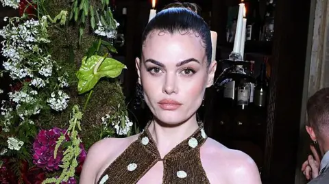 Getty Images Model Charli Howard poses in a gold sparkly dress with white polka dots and her brown hair slicked back into a bun