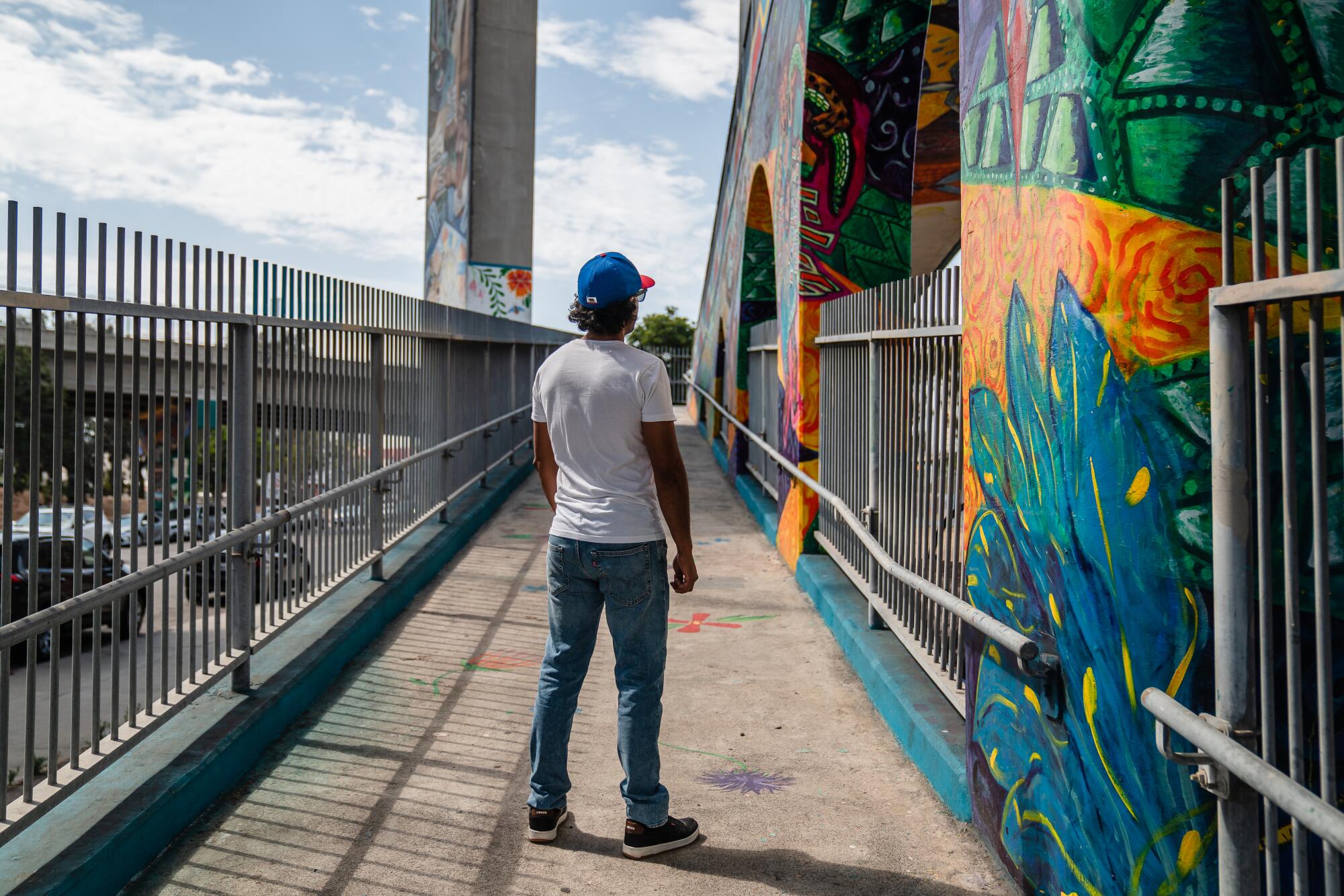 A person in a cap, white T-shirt and jeans, seen from behind, stands looking at a colorful mural