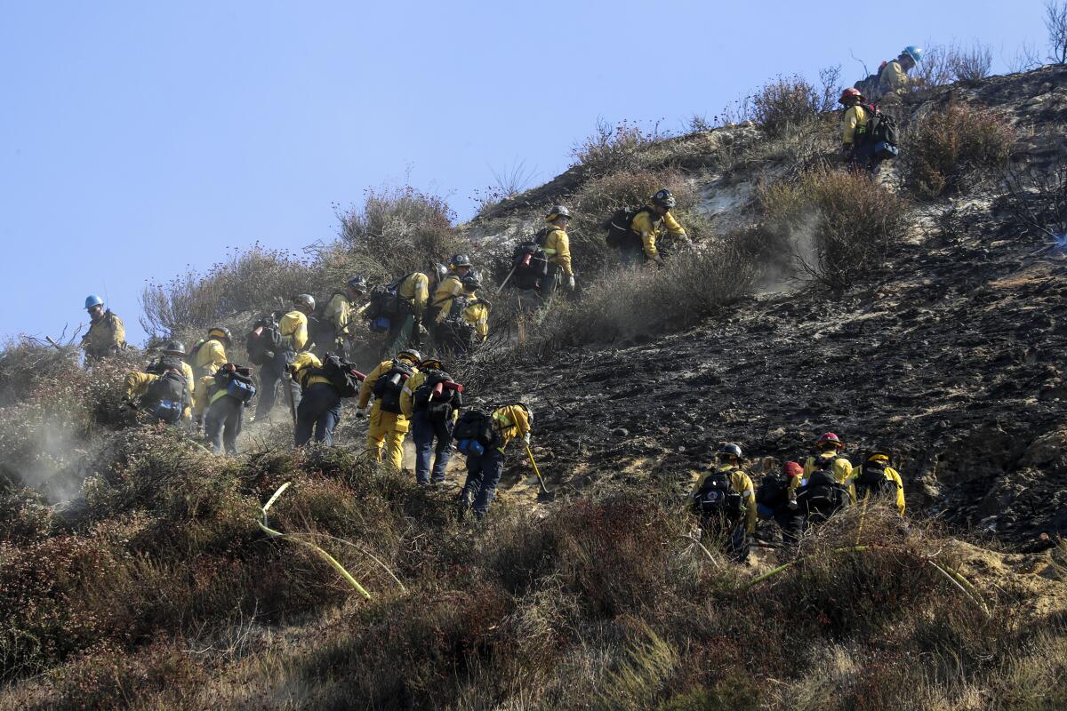 Firefighters clear brush and mop up a hillside