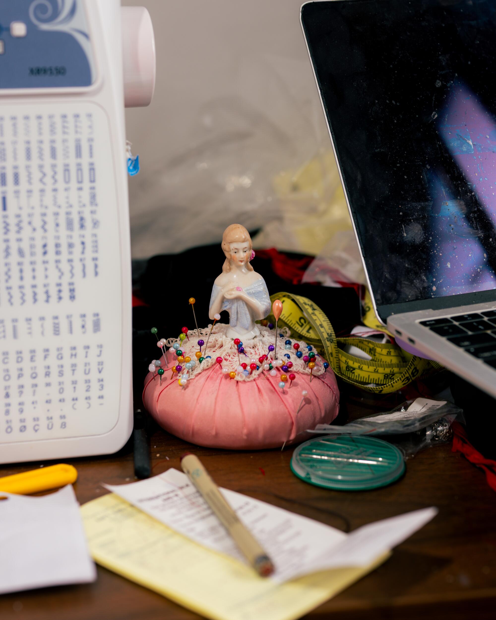 A porcelain doll pin sits on a cluttered desktop.