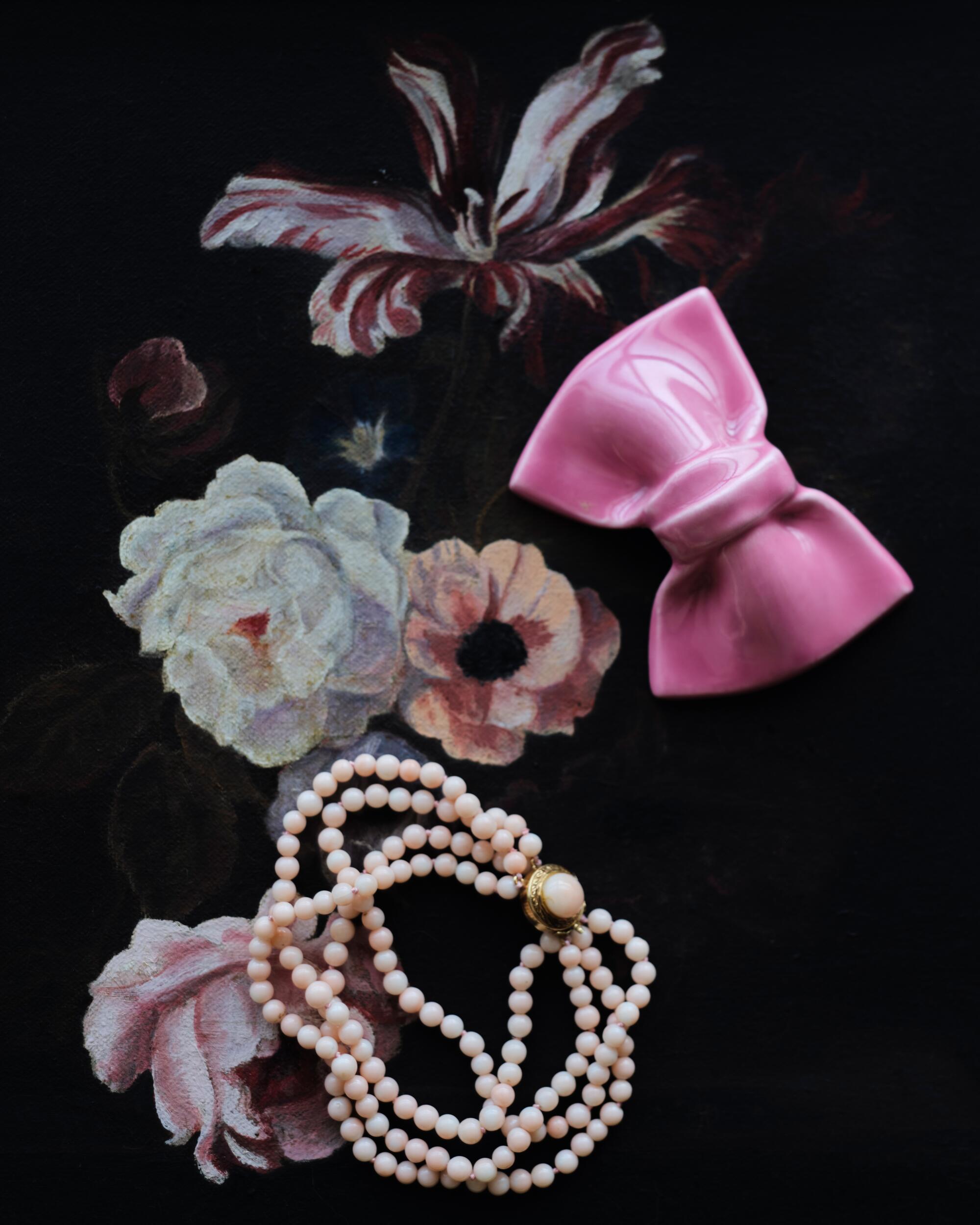 a beaded bracelet and pink ceramic bow on a dark floral background