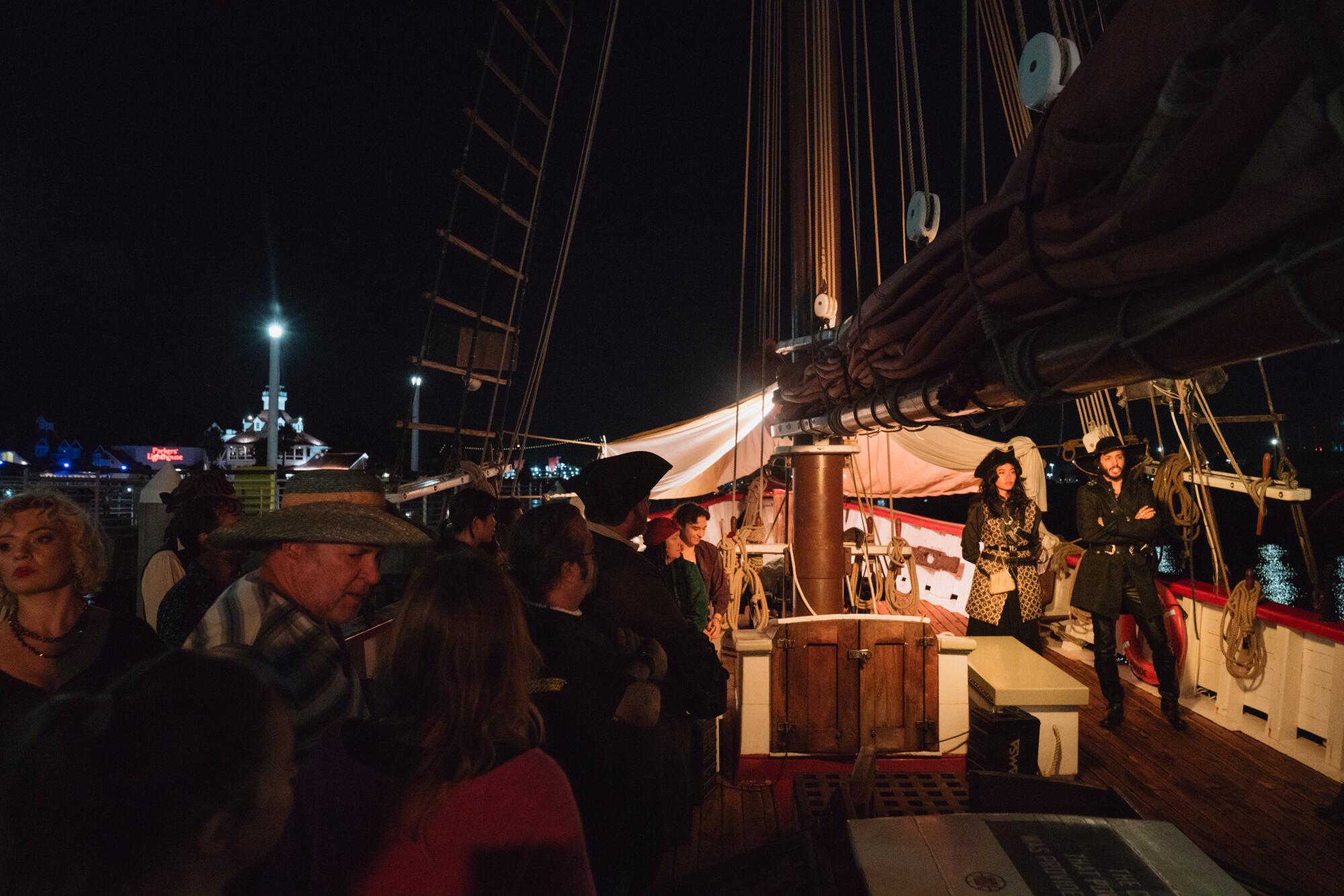Two actors in pirate outfits perform for an audience on a tall ship.