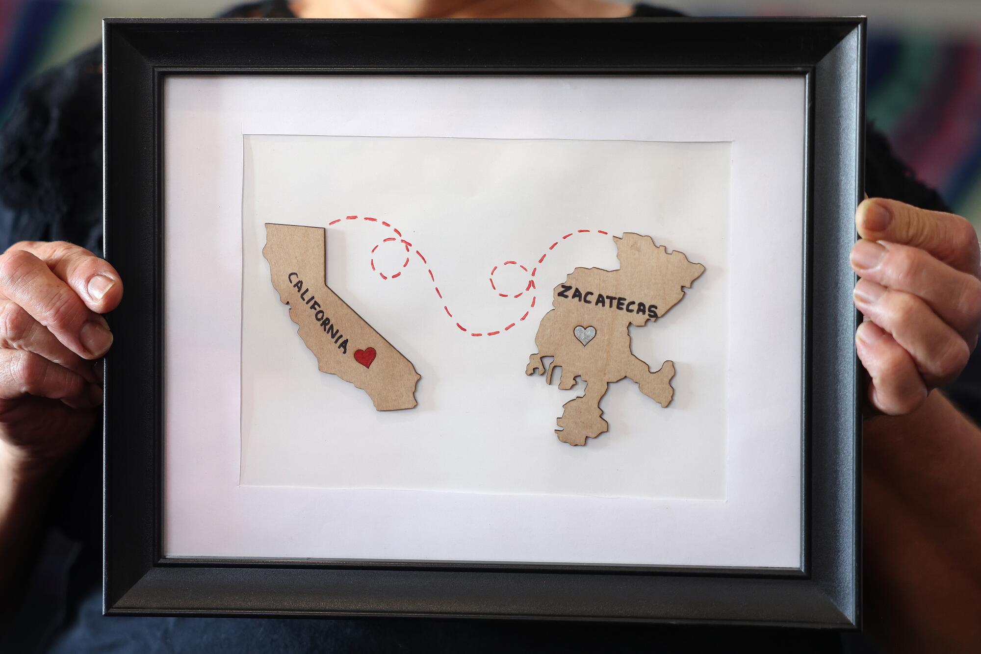 A person holds a framed piece of art showing the states of California and Zacatecas