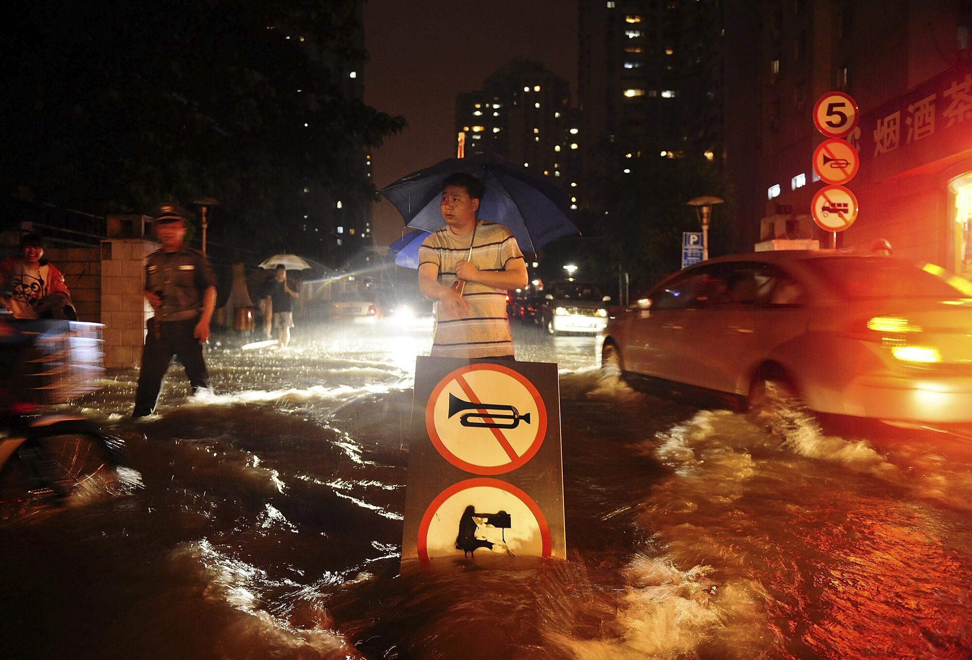 A man uses a signboard to signal motorists driving through a flooded street in China.