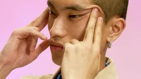 Swatch Close-up shot of a young Asian man with pulling the corners of his eyes up with both hands.