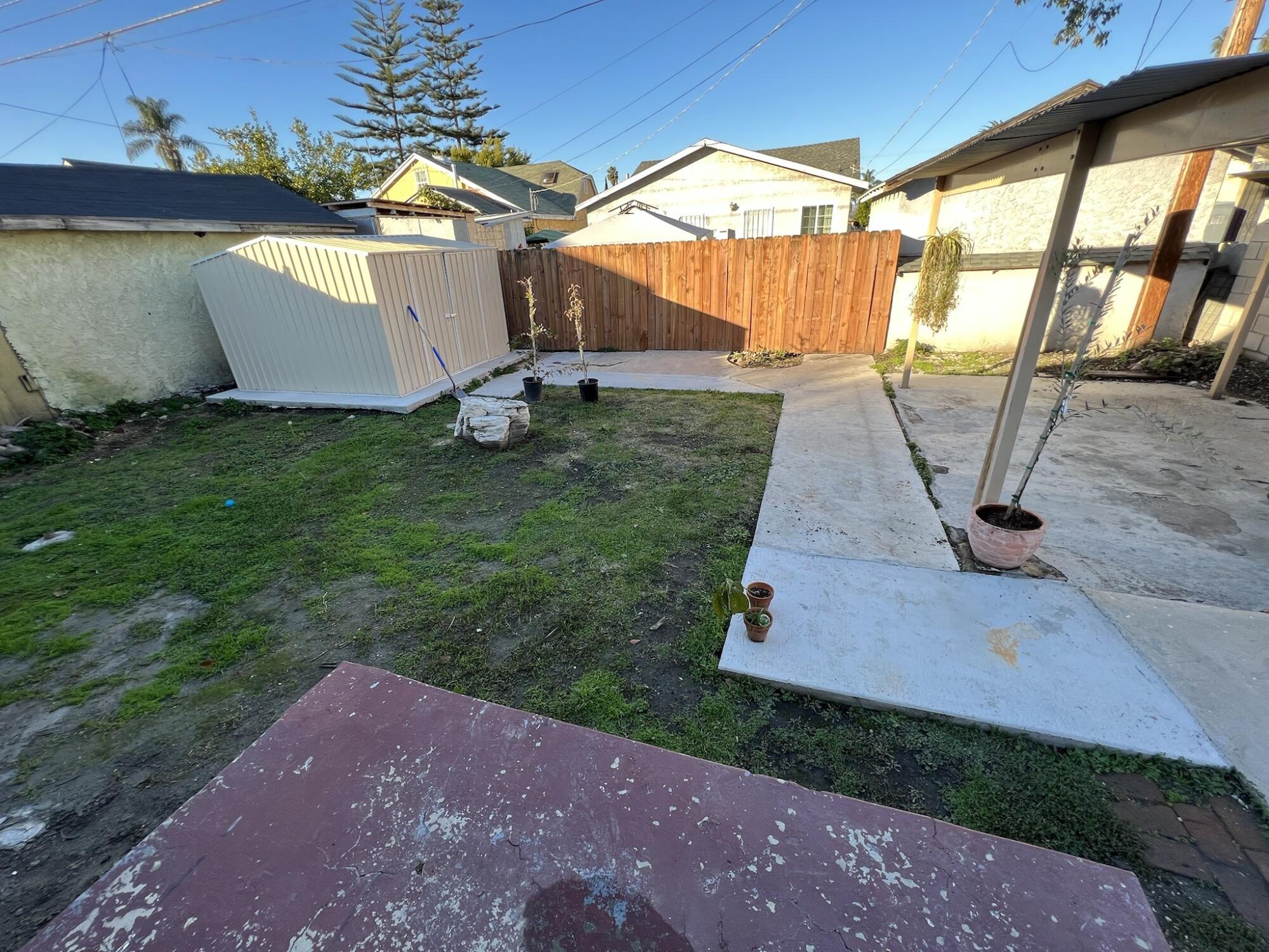 A backyard with patchy brown lawn and concrete.