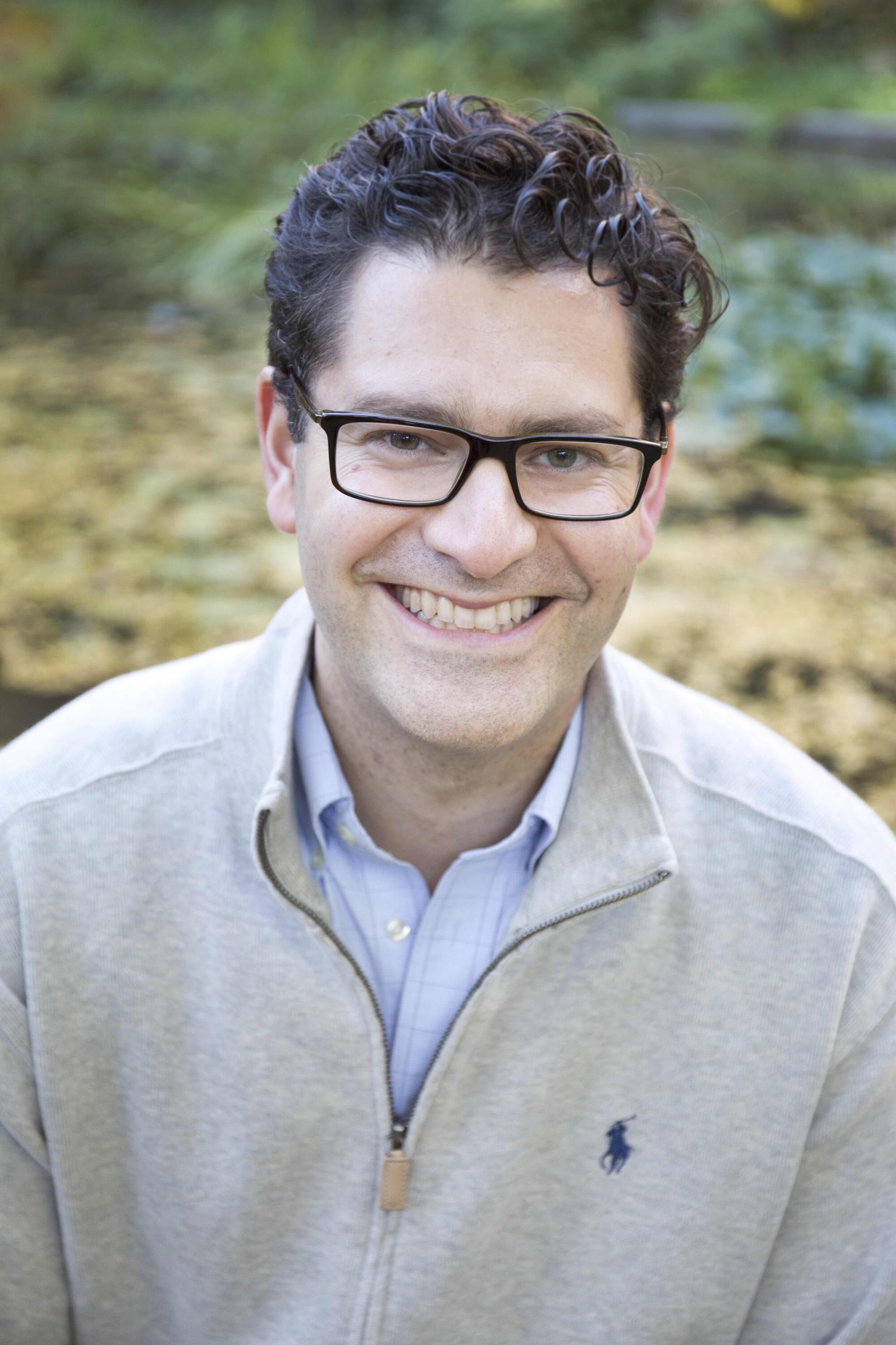 A photo of a man wearing glasses and smiling.