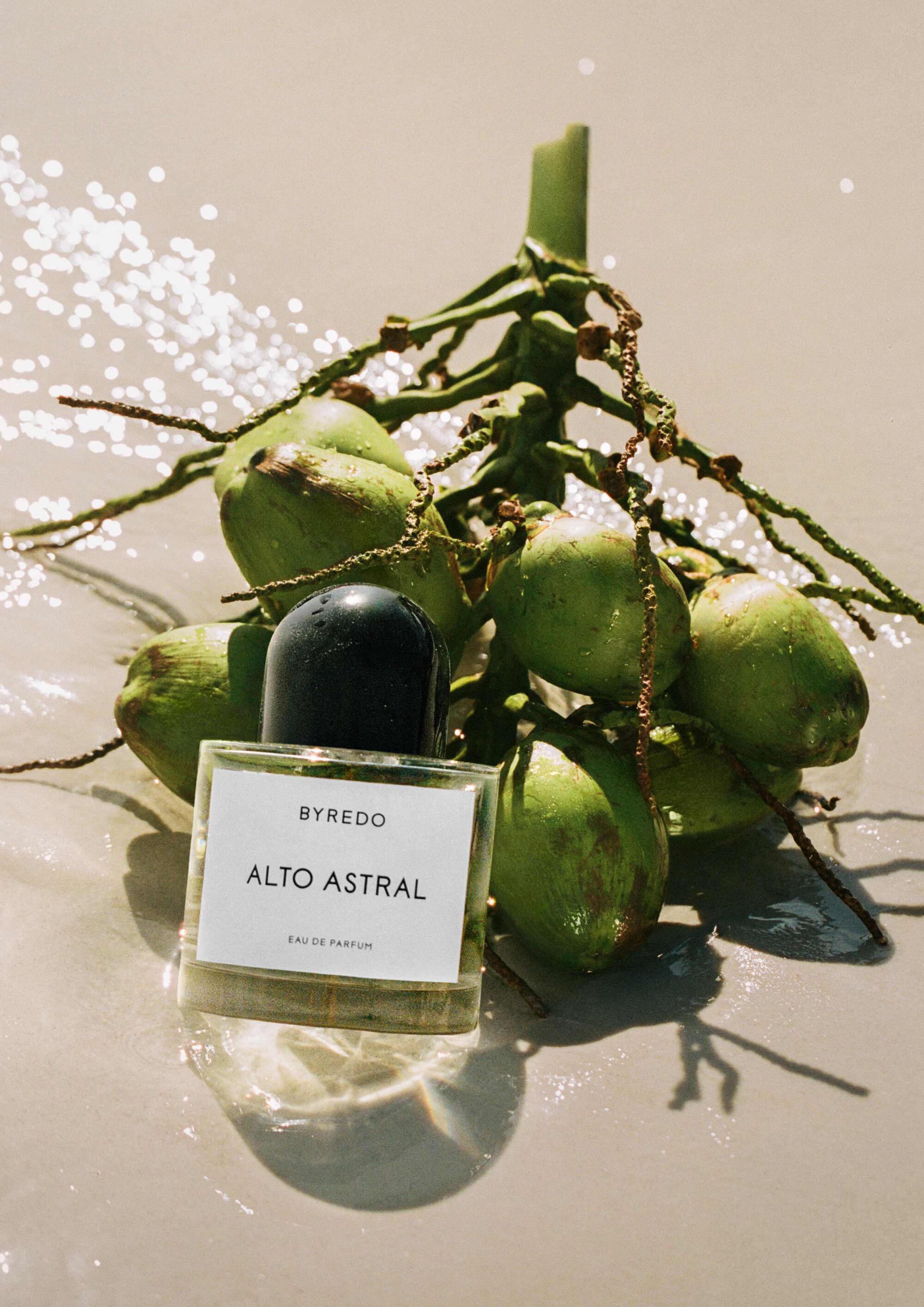 Byredo Alto Astral perfume resting next to a bunch of coconuts on the sand
