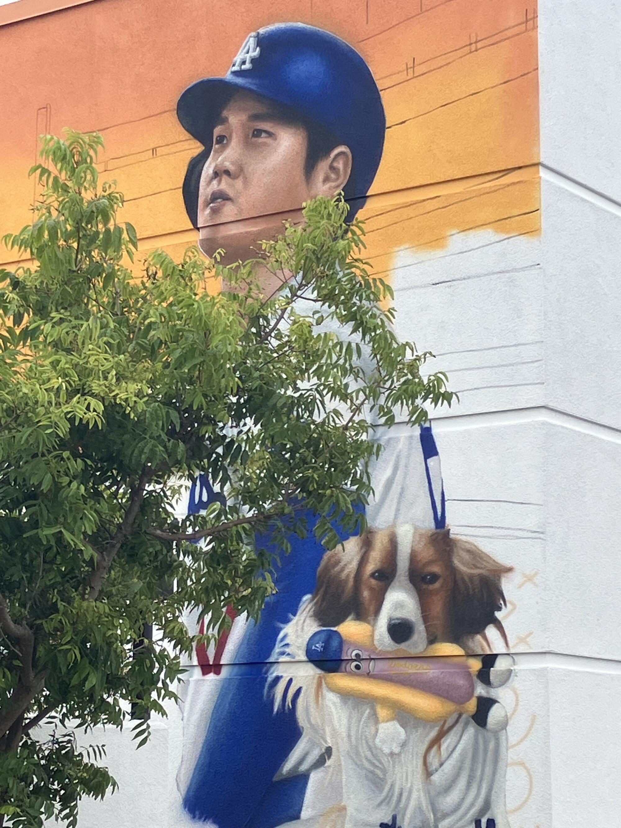 Shohei Ohtani and his dog Decoy are painted on a wall with a tree slightly blocking the view