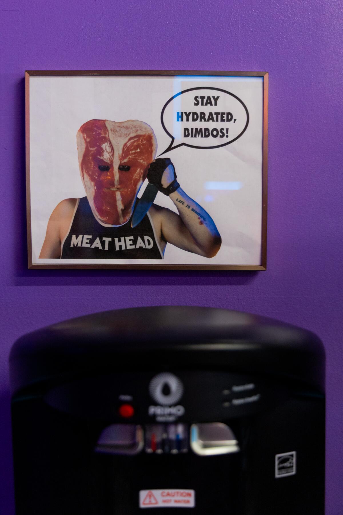 A "Stay hydrated, bimbos!" poster hangs above the water fountain.