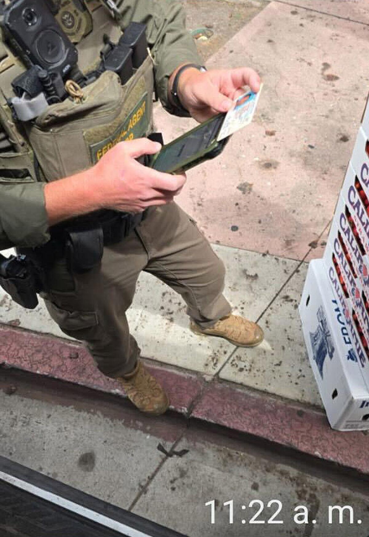 Image of a federal agent looking at identification outside of the Japanese American National Museum on Aug. 14.