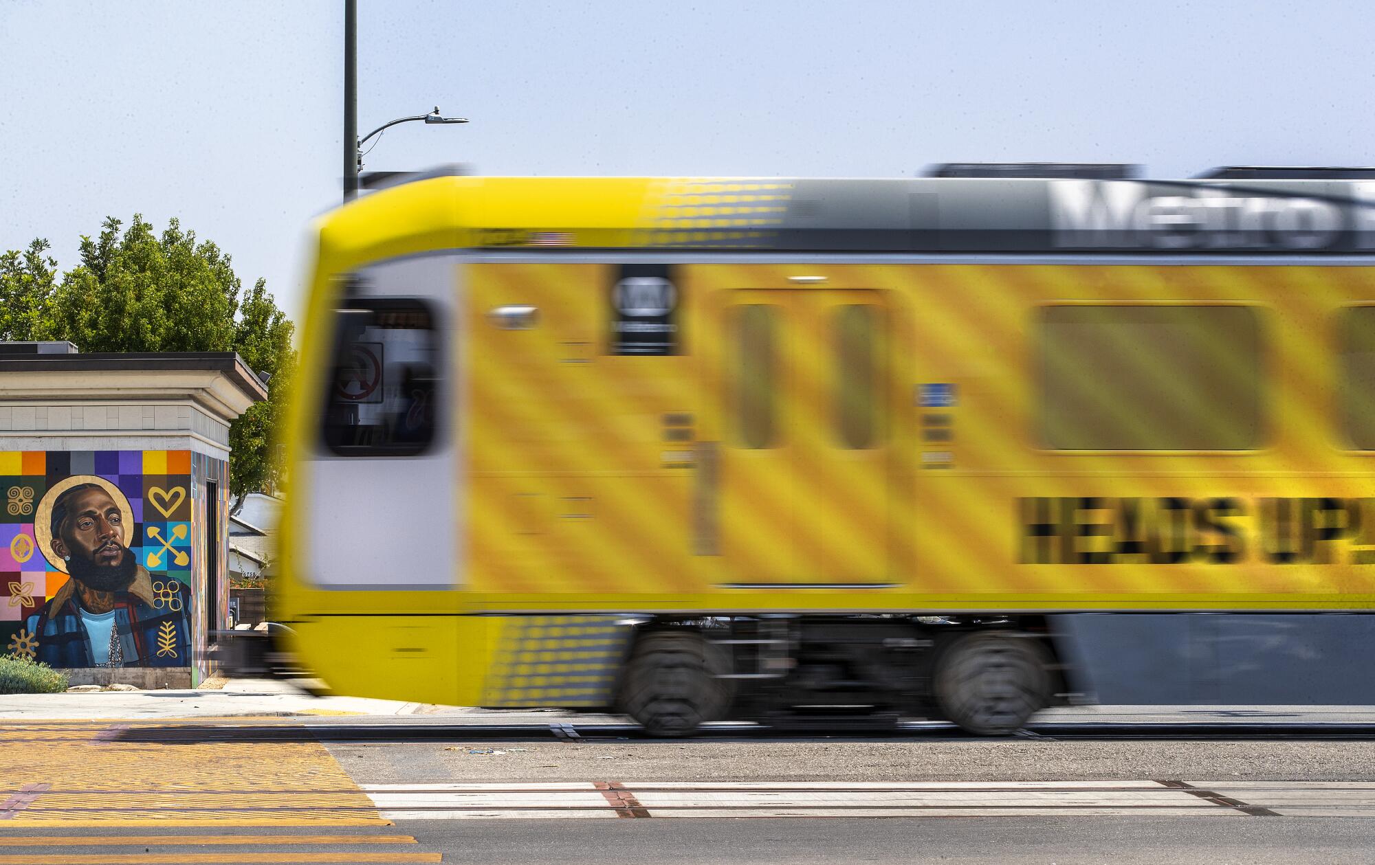 A yellow train near a mural of a man with a dark beard