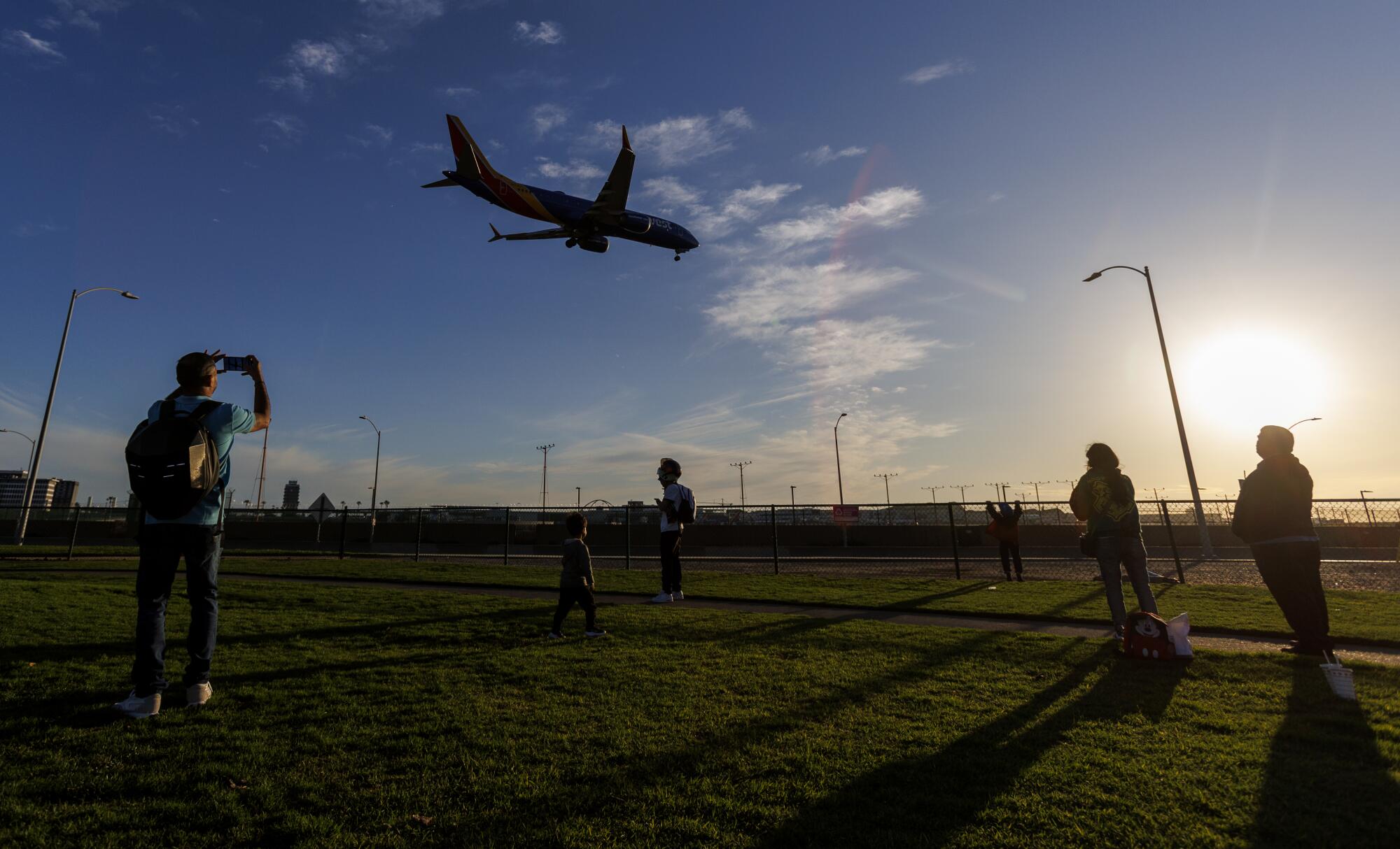 People standing on a grassy area look at a plane coming in for a landing