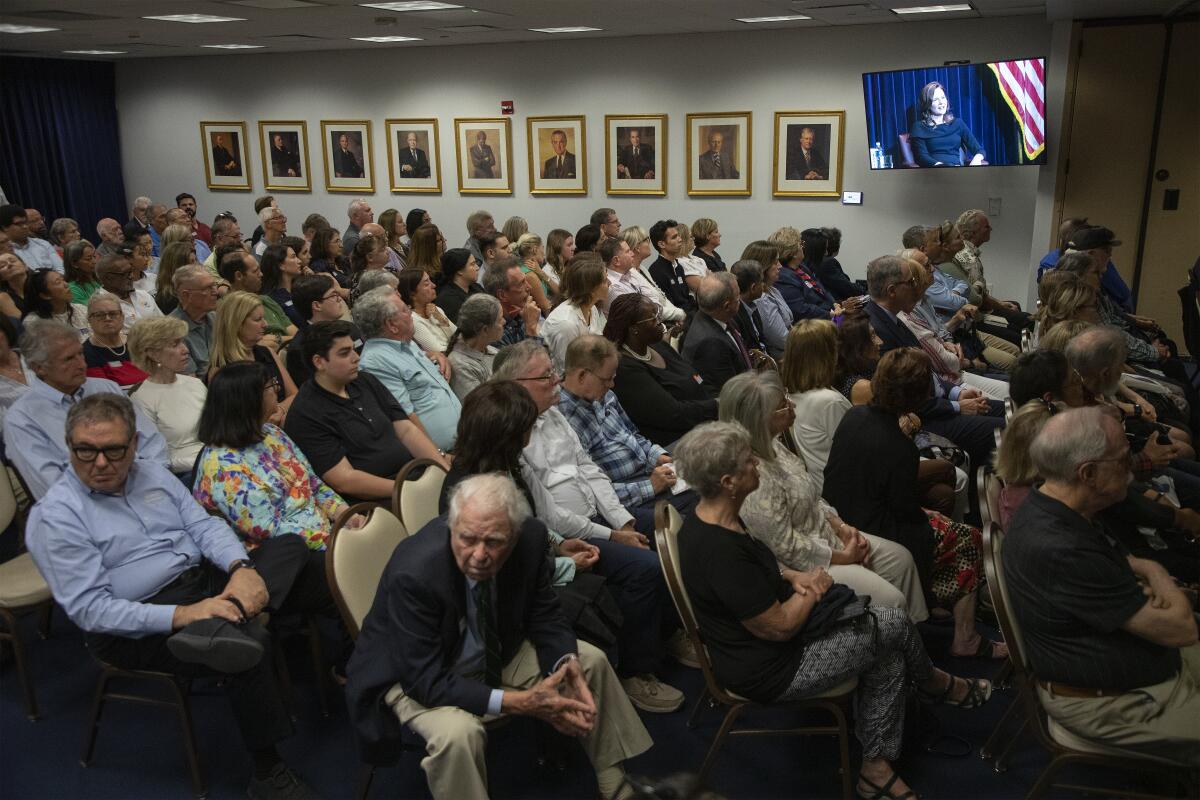 A packed room listens and watches monitors