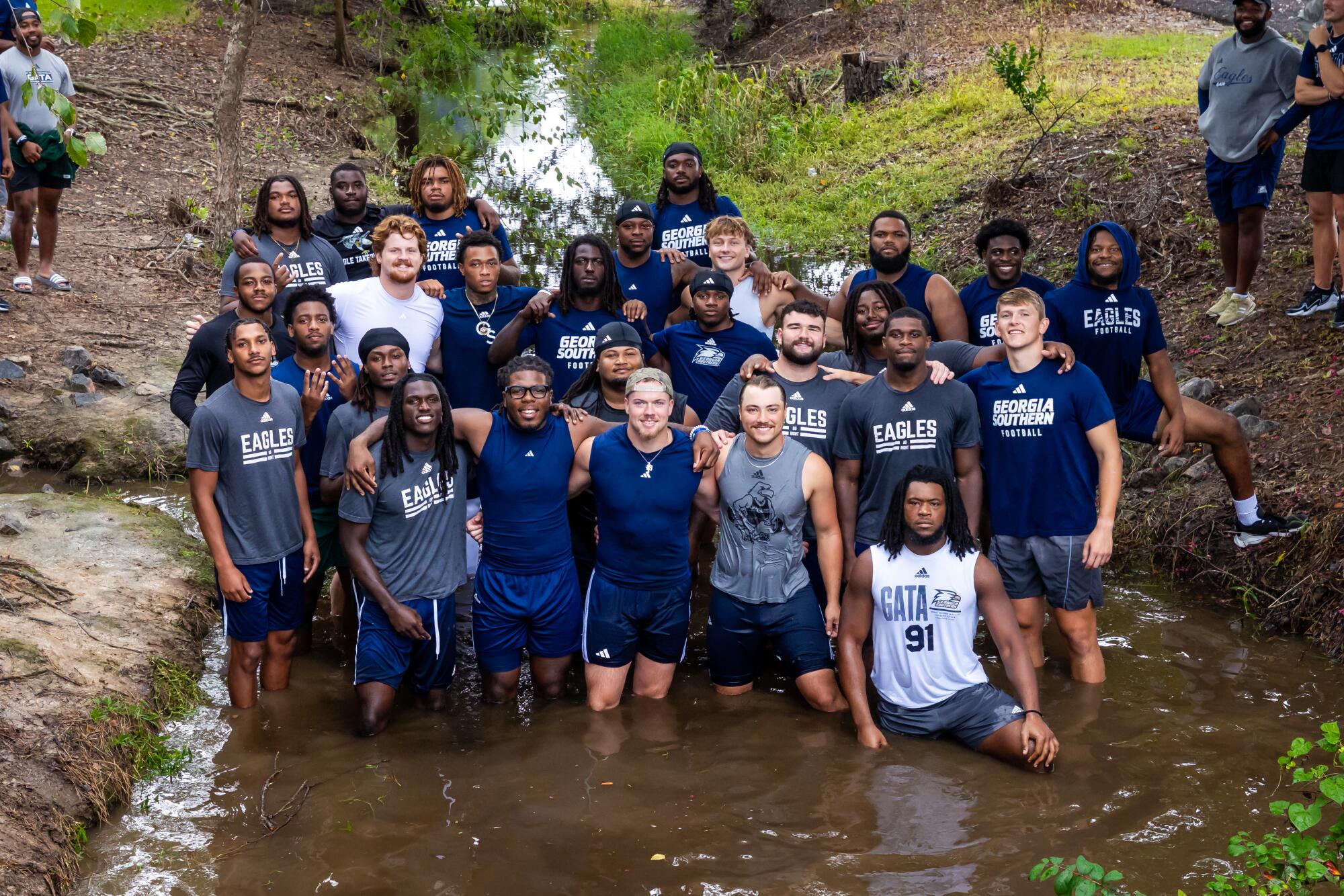 Georgia Southern football players stand in Beautiful Eagle Creek with their arms draped around each other's shoulders