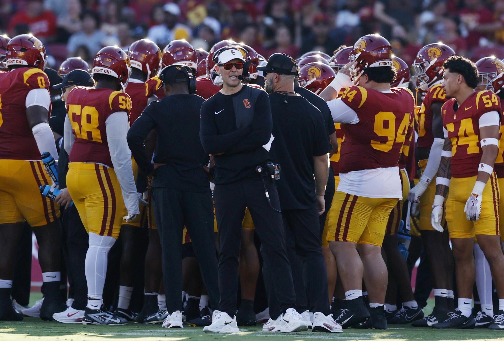 USC coach Lincoln Riley stands on the sideline alongside his players while talking into a headset during a game.