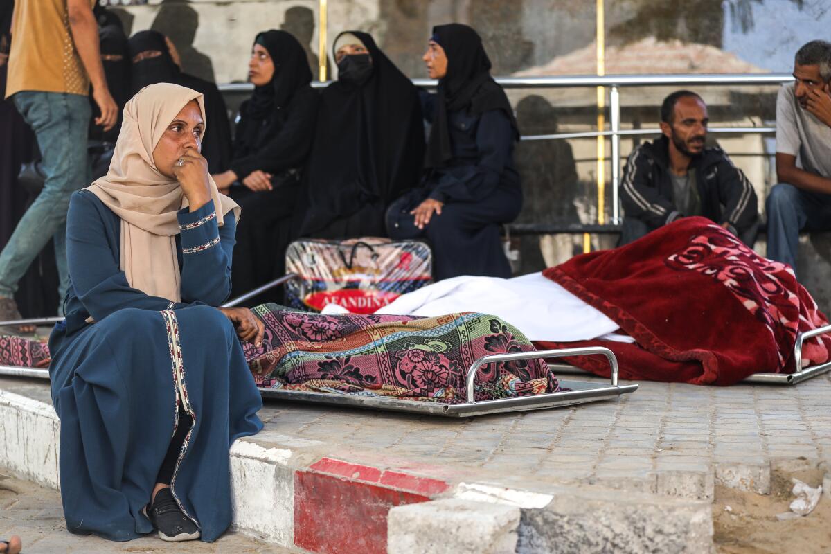 A Palestinian woman sits next to wrapped bodies on stretchers.