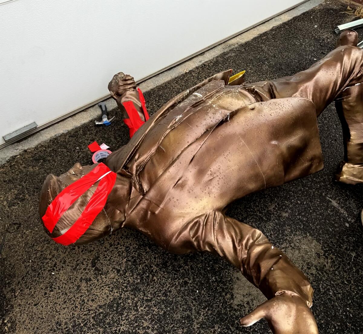 A bronze statue of President Trump with its broken head put back together with red duct tape. 