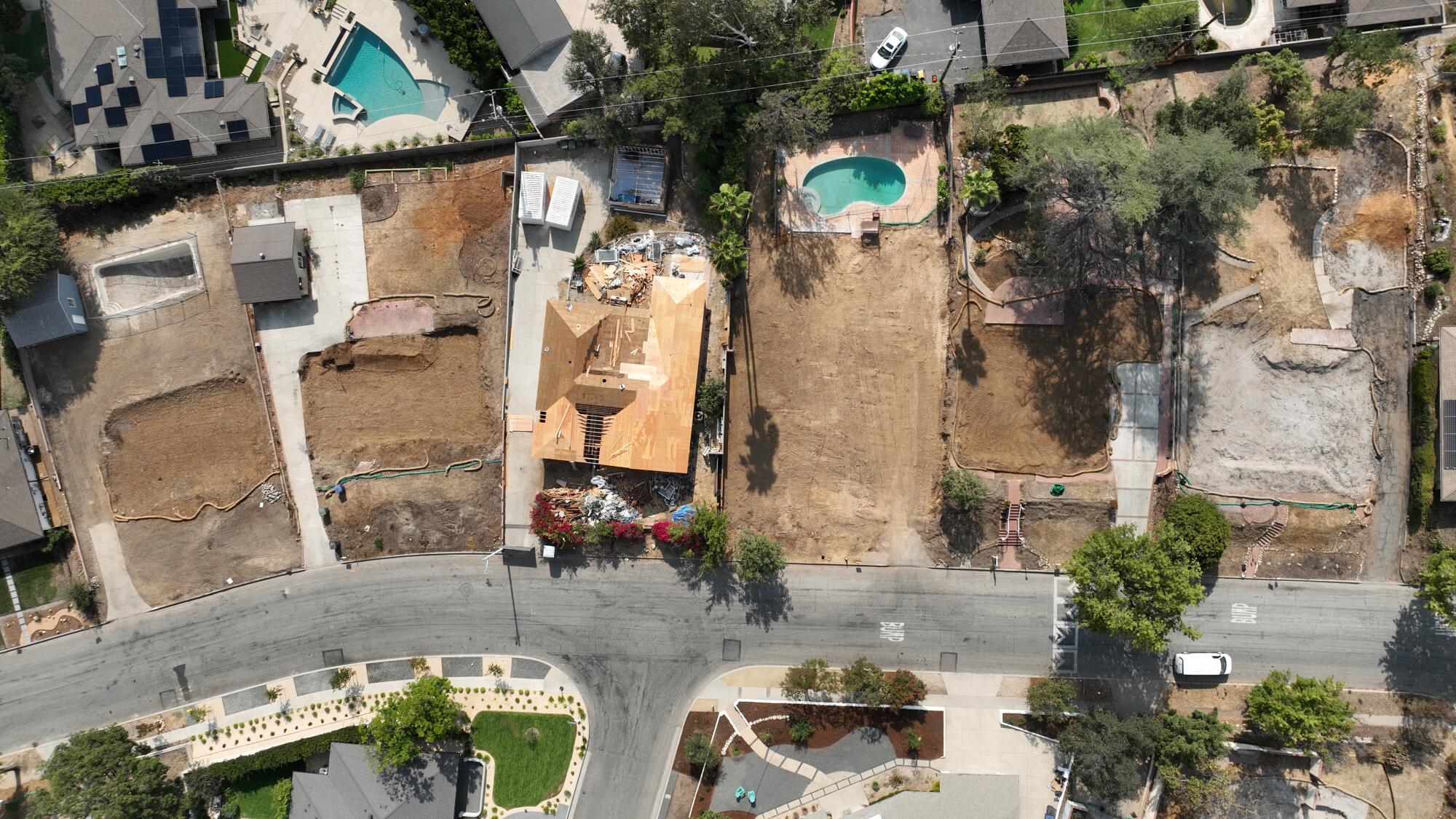 Aerial view of cleared properties and construction crews working on rebuilding a home in Altadena.