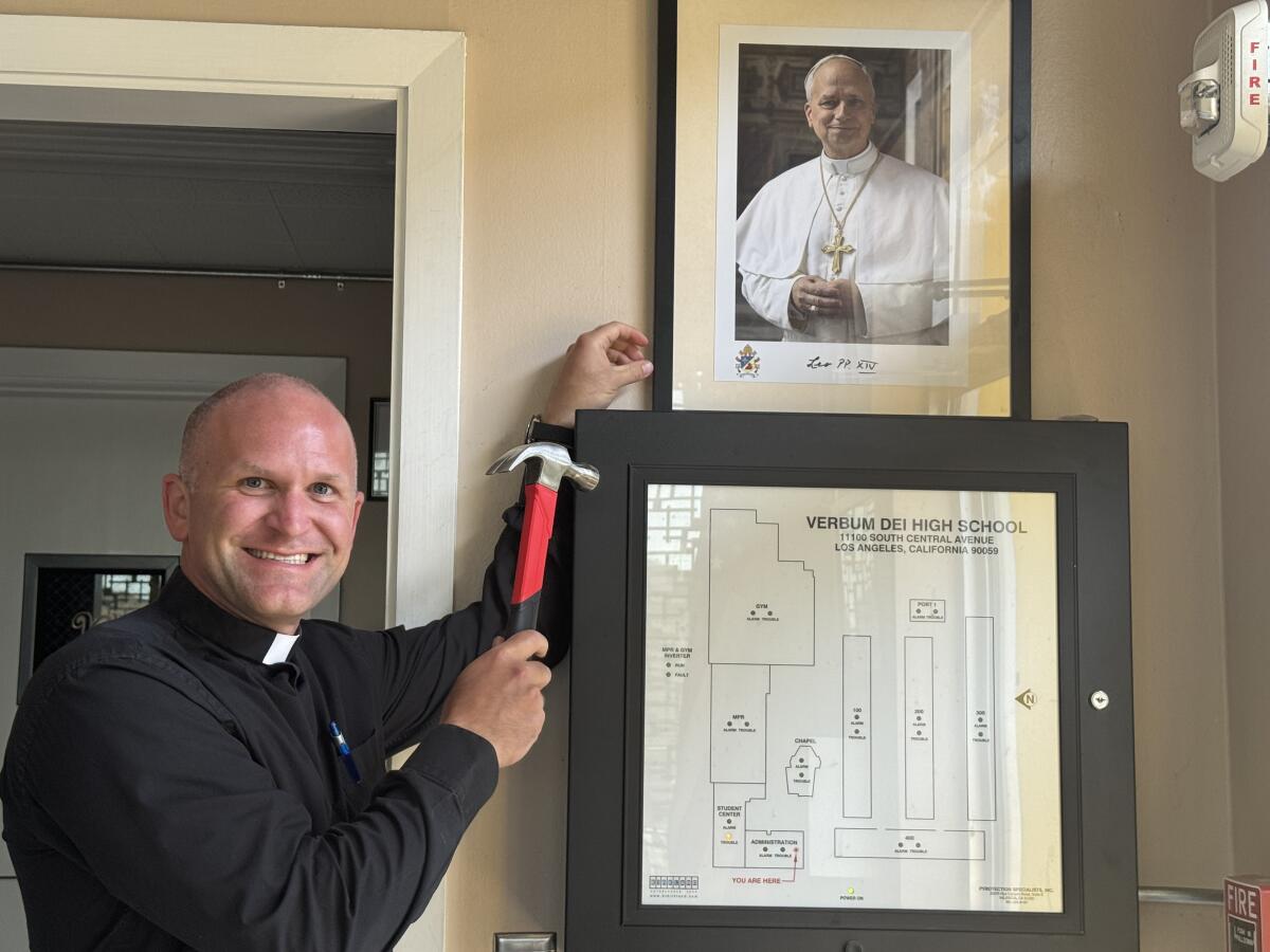 Father Travis Russell, president of Verbum Dei High, poses for a photo after hanging a picture Pope Leo XIV.